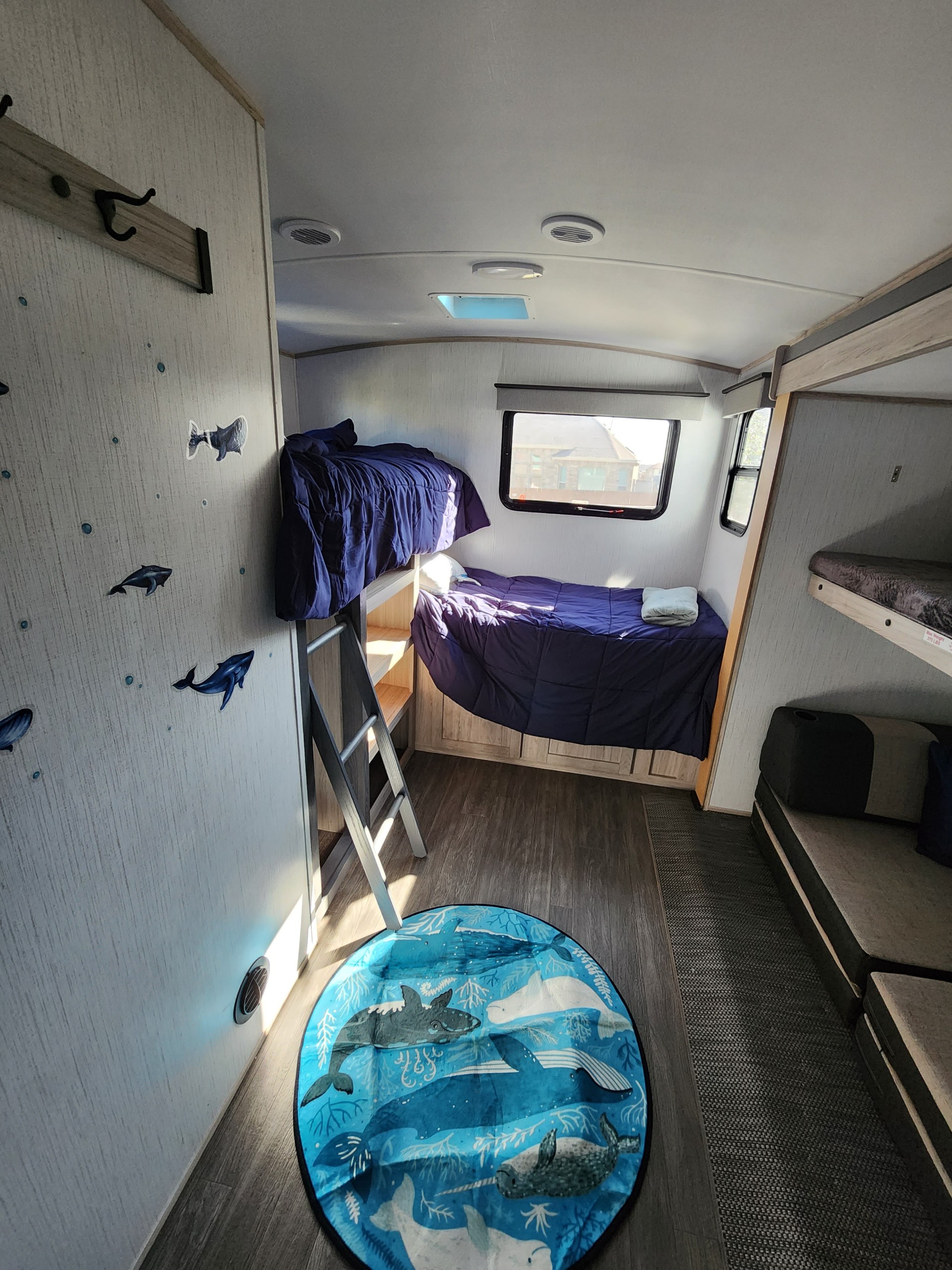 RV rental bunkhouse featuring two sets of beds, a ladder, and a vibrant blue ocean-themed rug on the floor.. Twilight RVS Signature 2022
