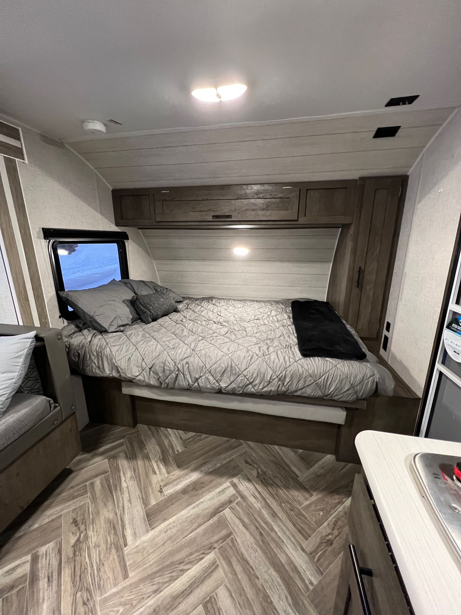 Inside an RV rental: a cozy bedroom with a bed, window, and wood-paneled cabinets. Features a herringbone floor.. Forest River Other 2021