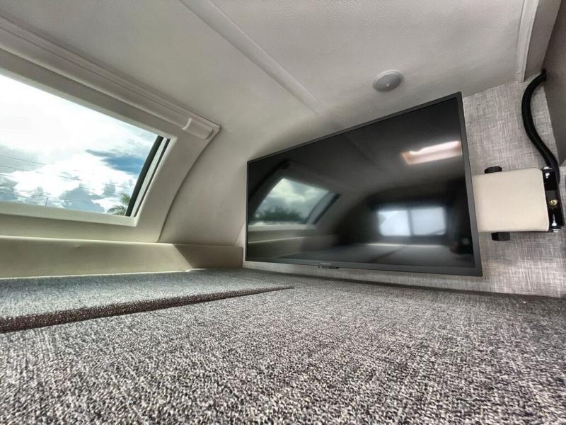 Inside an RV rental: a carpeted bunk area with a large window and mounted flat-screen TV.. Thor Quantum LC 2022