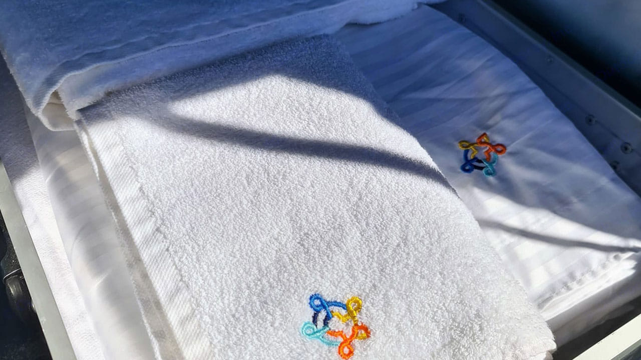 Fresh white towels and bedding with colorful embroidered logos, neatly folded for your comfortable RV rental.. Carado T338 2022