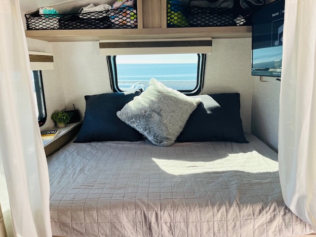 Cozy RV rental bedroom with a stunning ocean view, perfect for beach getaways and comfortable travel.. Forest River Rockwood Geo Pro 2023