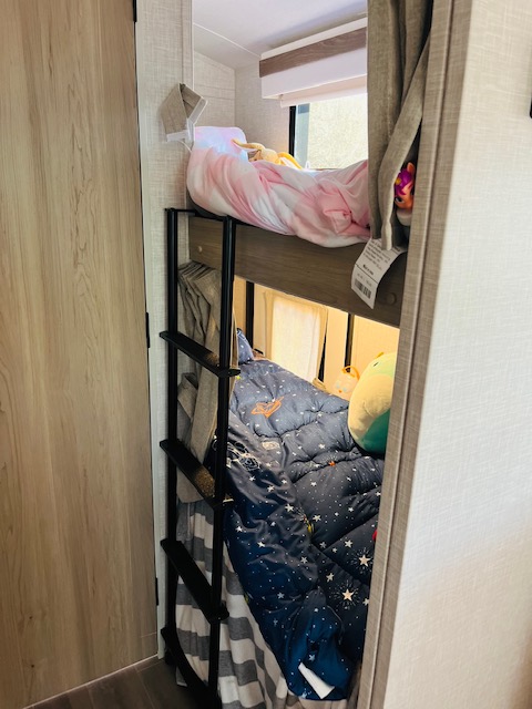 Inside an RV rental, two bunk beds are ready with comfy blankets; pink on top, space-themed blue on bottom.. Forest River Rockwood Geo Pro 2023