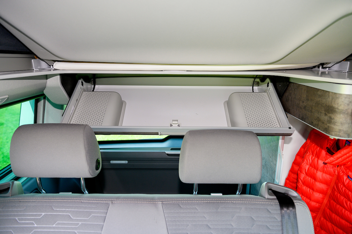 Inside an RV rental, showing rear seats, an open overhead storage area with bins, and a tucked-away pop-top bed.. Volkswagen California Ocean 2024