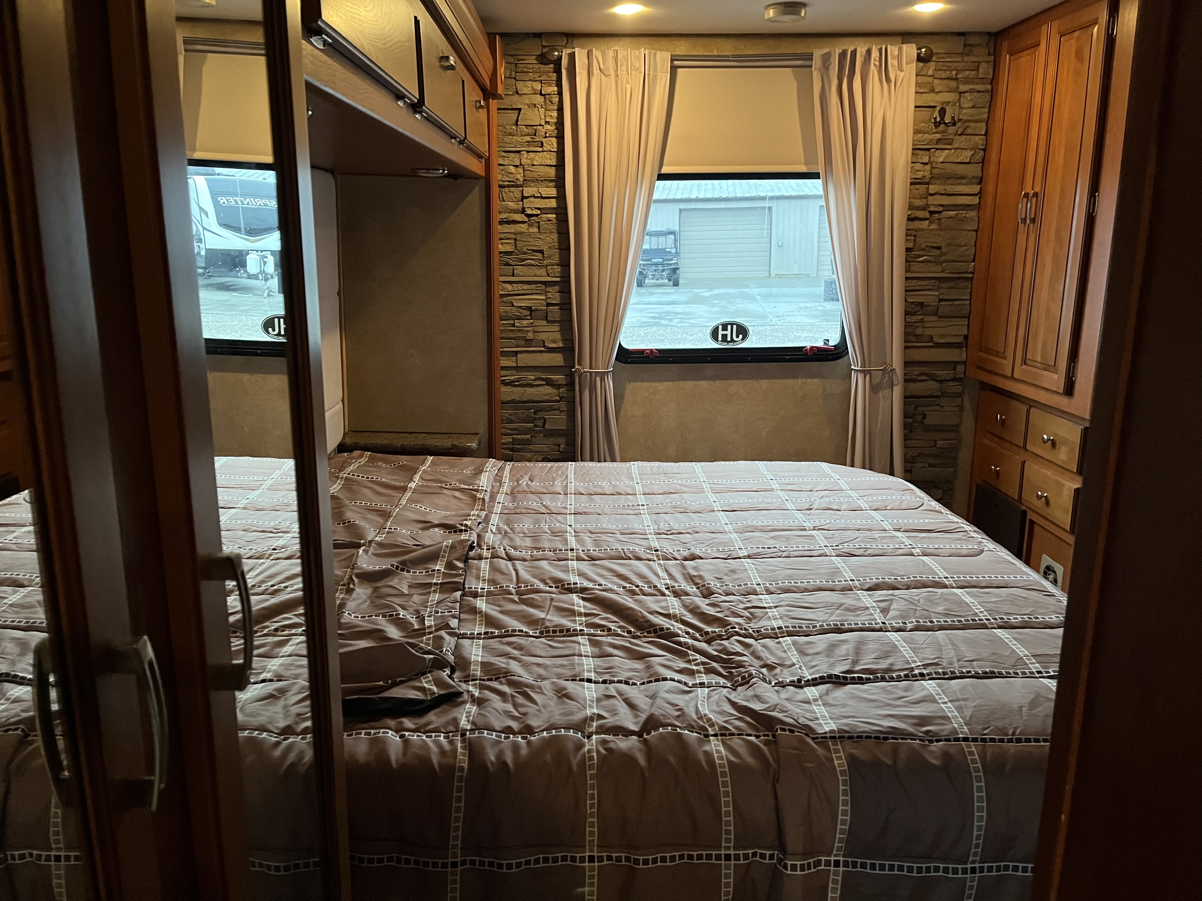 Cozy RV rental bedroom with a brown patterned bed, stone accent wall, wood storage, and a window showing an exterior view.. Forest River Georgetown M373DS 2011
