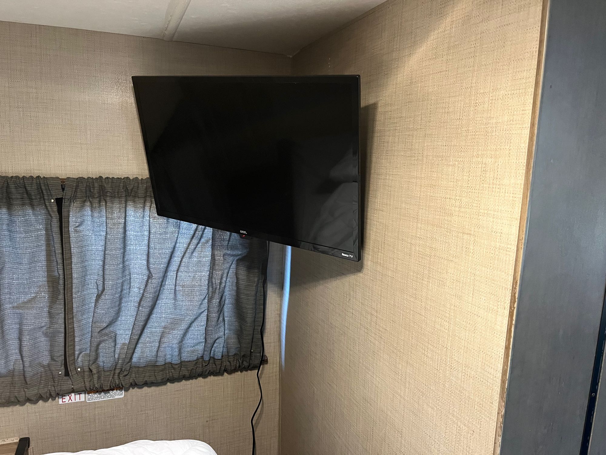 RV rental interior featuring a wall-mounted TV, window with drawn curtains, and an "EXIT" sign, providing a comfortable space.. Thor Majestic 2018