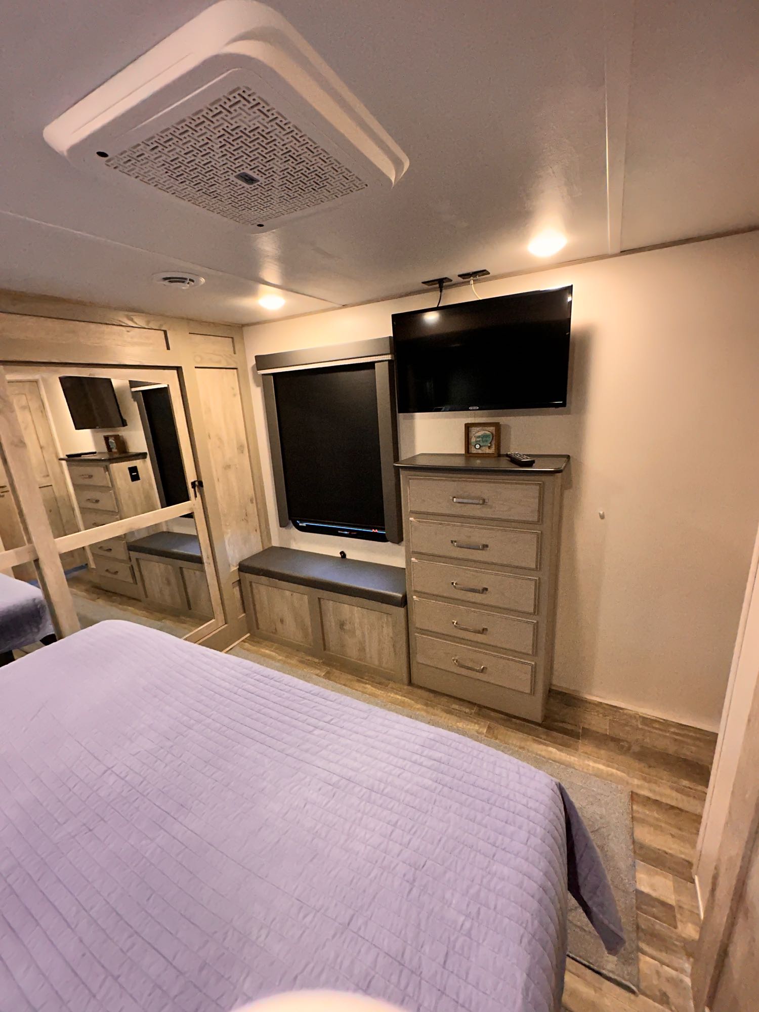 Cozy RV rental bedroom with a purple-quilted bed, TV, dresser, window seating, and ceiling AC unit.. Keystone RV Alpine 2022