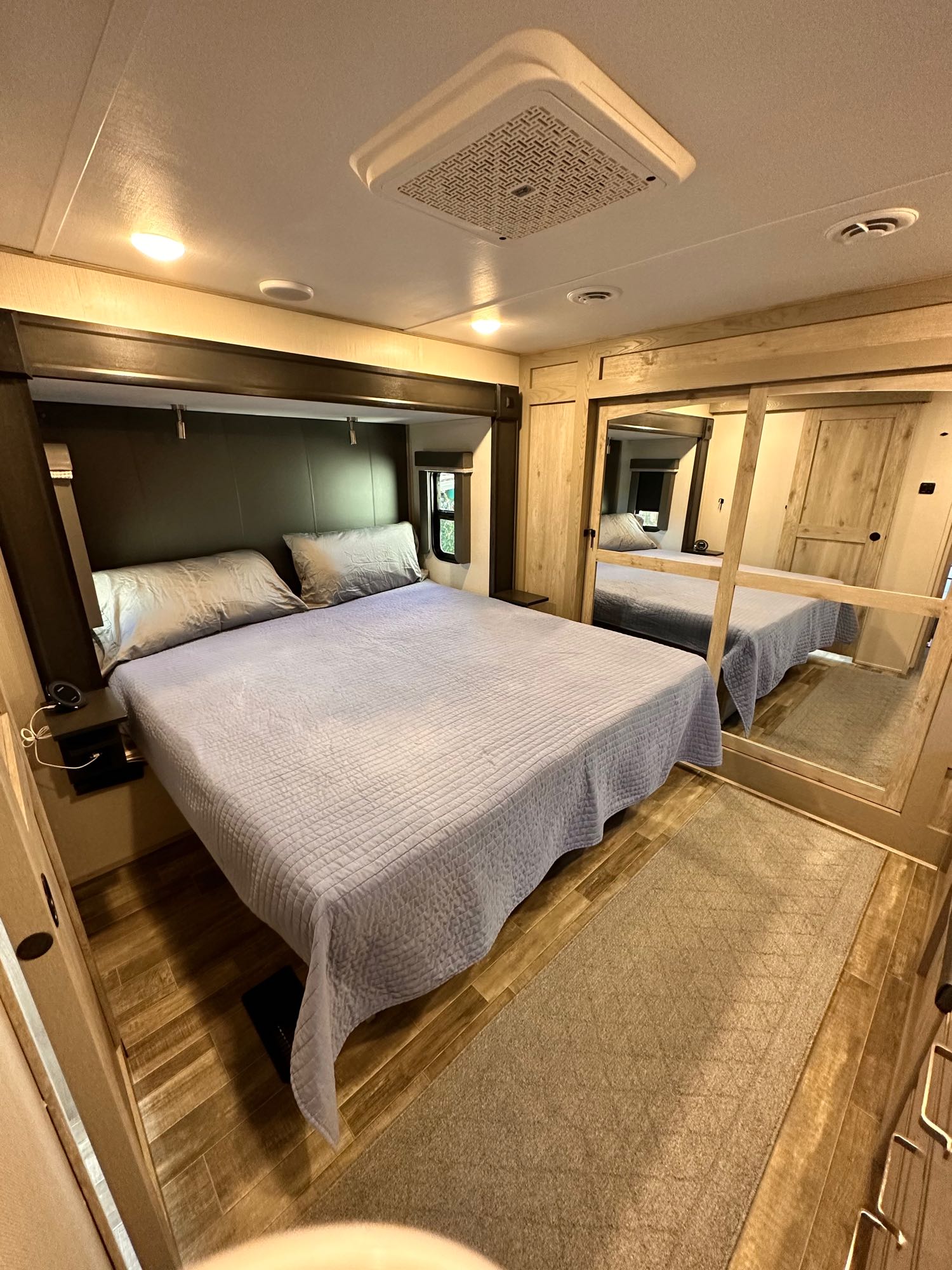 Comfortable RV rental bedroom featuring a bed with light blue quilt, mirrored closet, and wood flooring for mobile living.. Keystone RV Alpine 2022