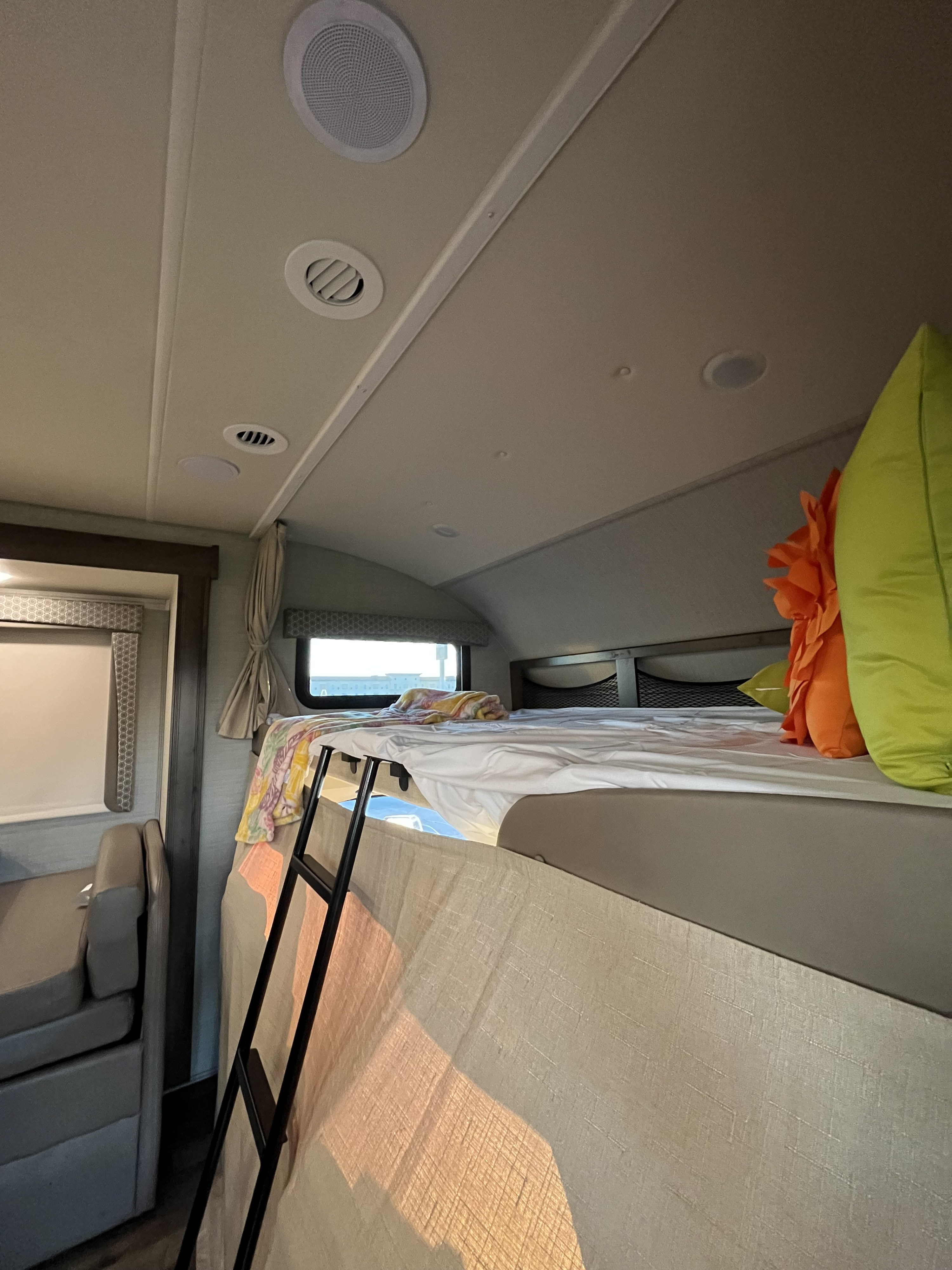 RV rental interior: looking up at the overhead bunk bed with ladder, bright window, and ceiling vents/speakers.. Jayco Greyhawk 2020