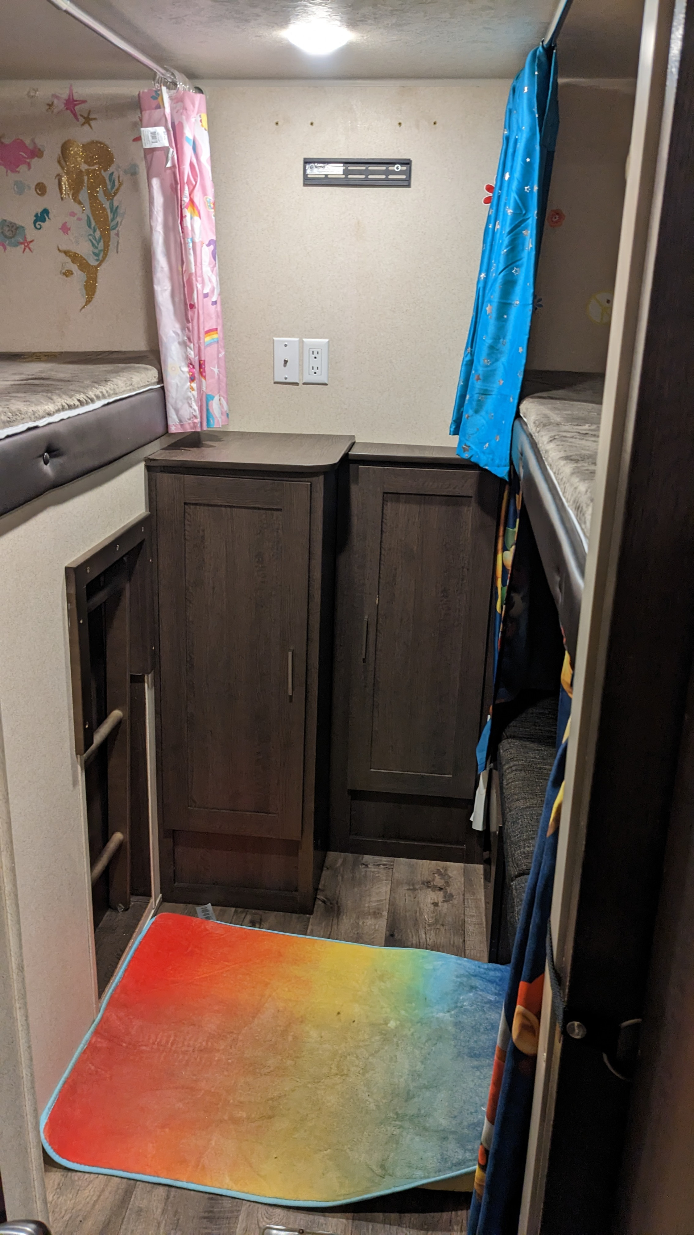 This rv rental shows bunk beds with privacy curtains (pink & blue), small cabinets, and a colorful rug, offering cozy, compact living.. Forest River Salem 2018