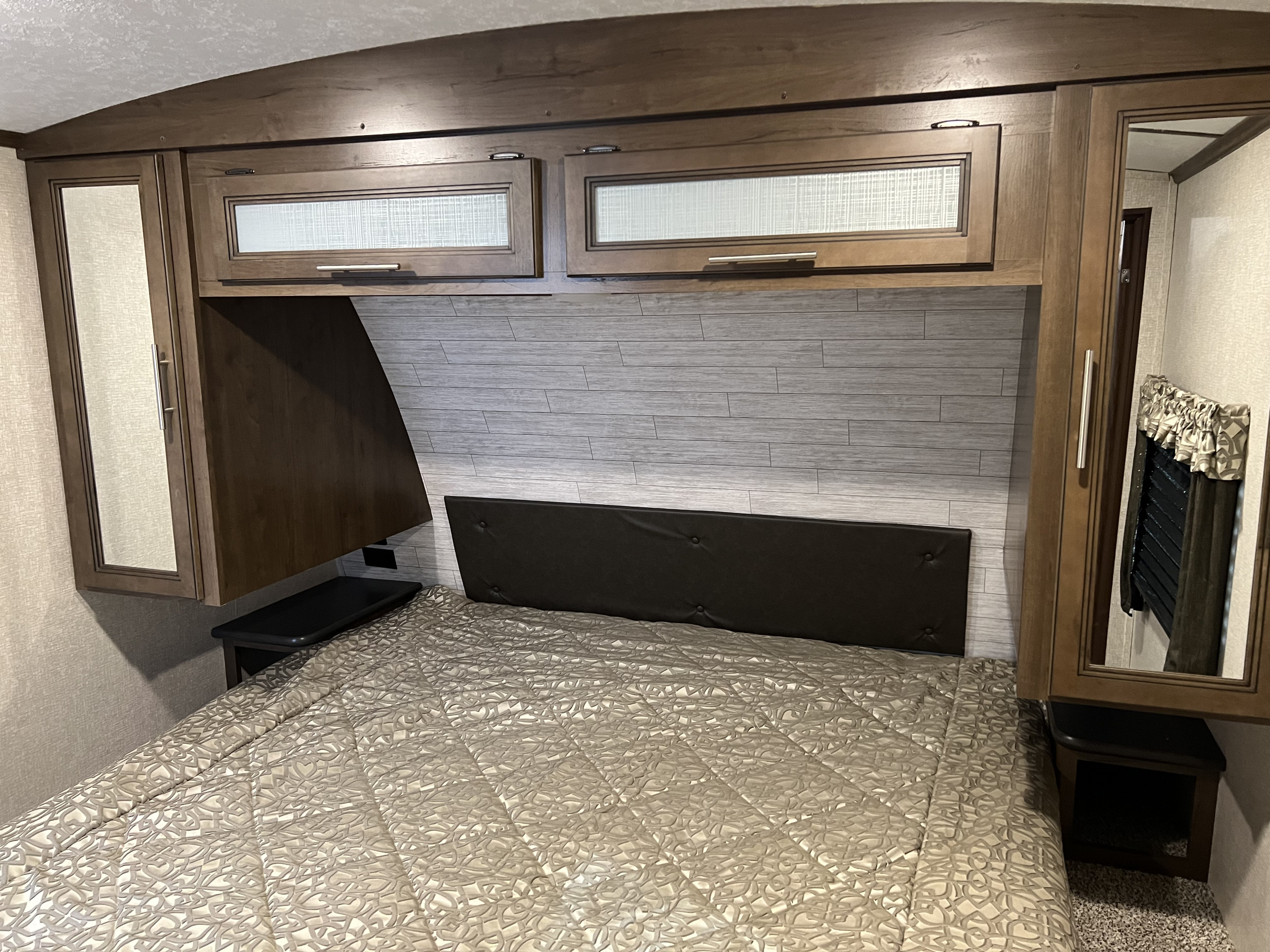 Inside an **RV rental**, this cozy **bedroom** boasts a dark headboard, wood-paneled walls, overhead cabinets, and a comfy bed.. Cougar 29RLK 2020
