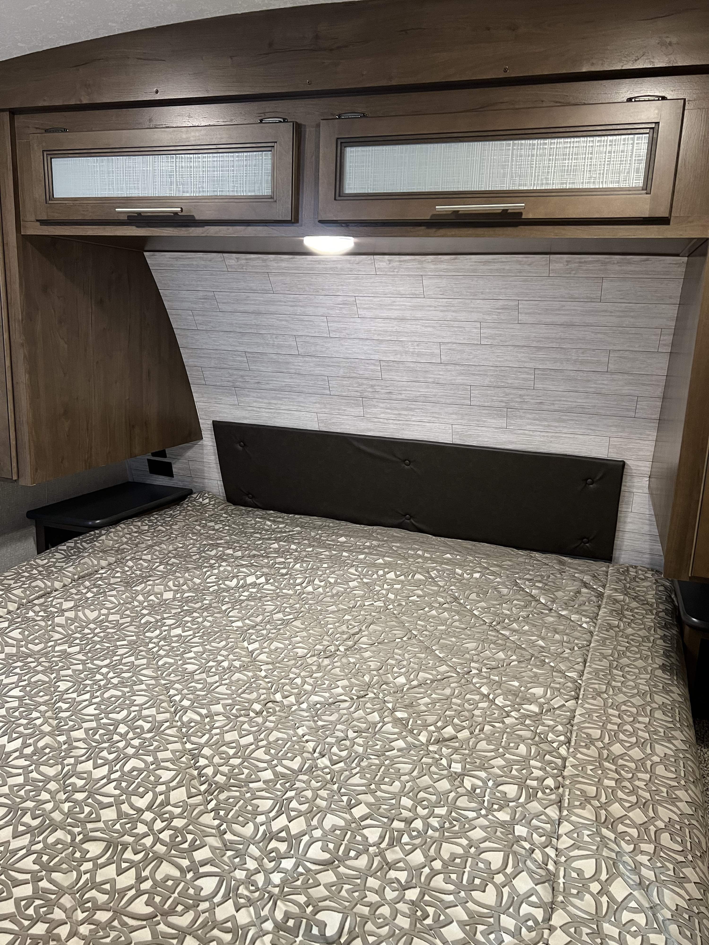 Inside this RV rental, find a modern bedroom: bed with patterned comforter, tufted headboard, and overhead storage.. Cougar 29RLK 2020