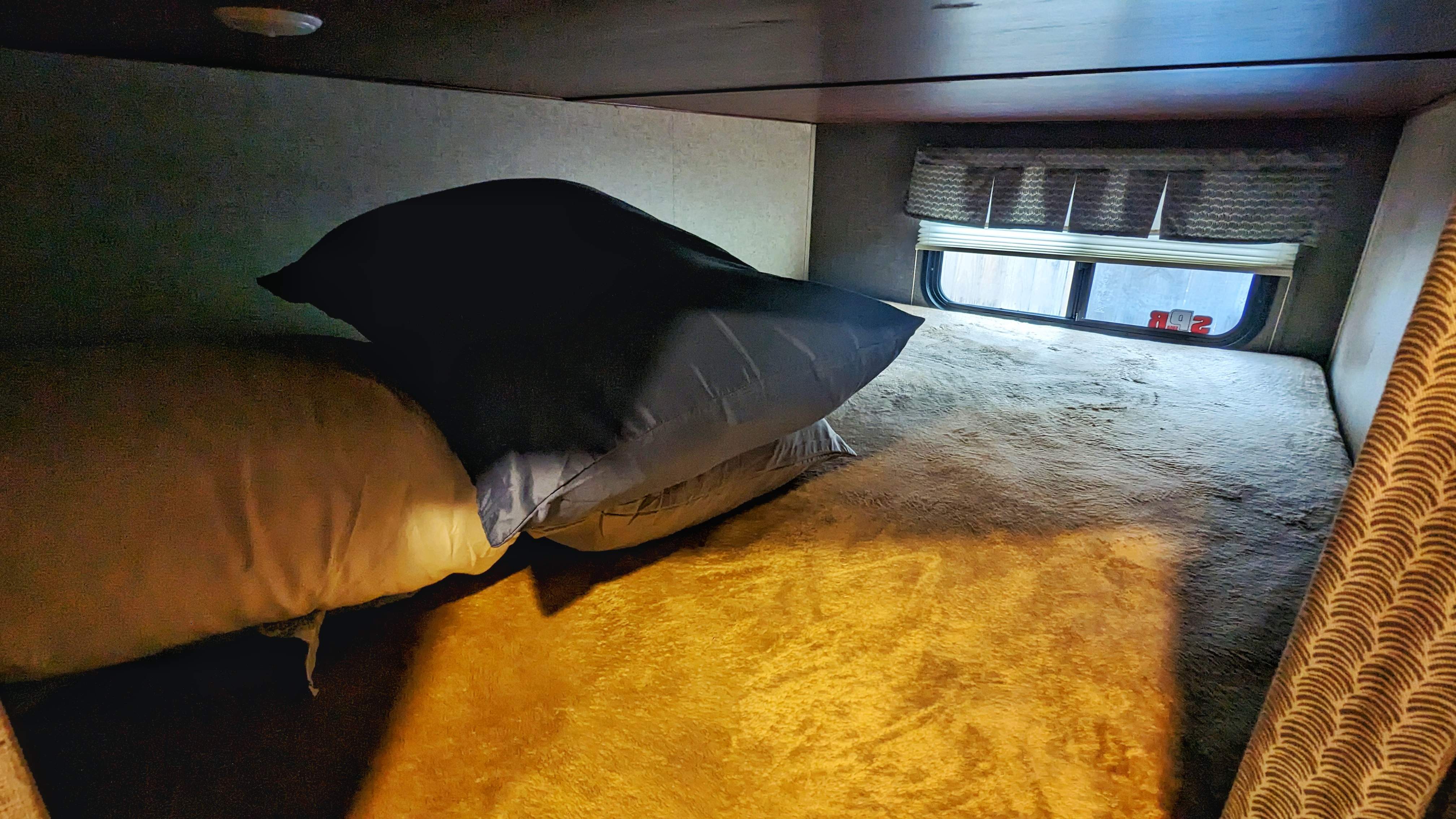 Cozy RV rental bunk bed with soft blankets & pillows. Features a window, ideal for travel & camping comfort.. Heartland RVs Mallard 2018