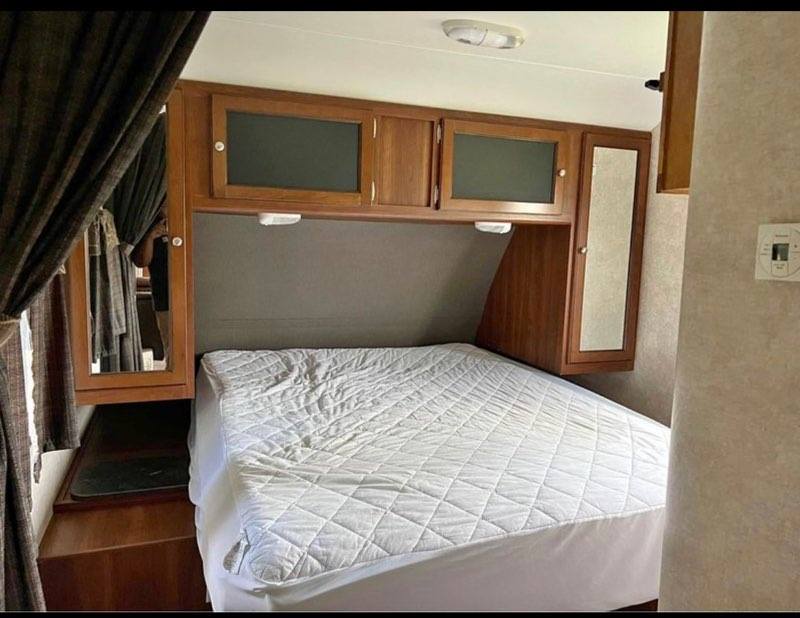 RV rental: Bedroom interior features a white bed, wood overhead cabinets, and a mirrored closet for a cozy sleeping area.. Keystone Bullet 2015