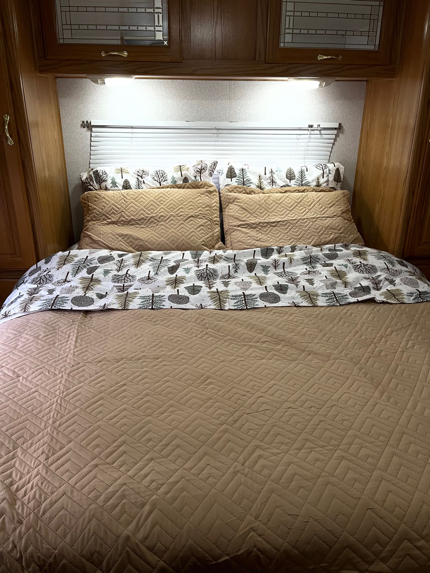 Cozy RV rental bedroom with patterned tree bedding, quilted comforter, and overhead wood cabinets.. Shasta Cheyenne 2001