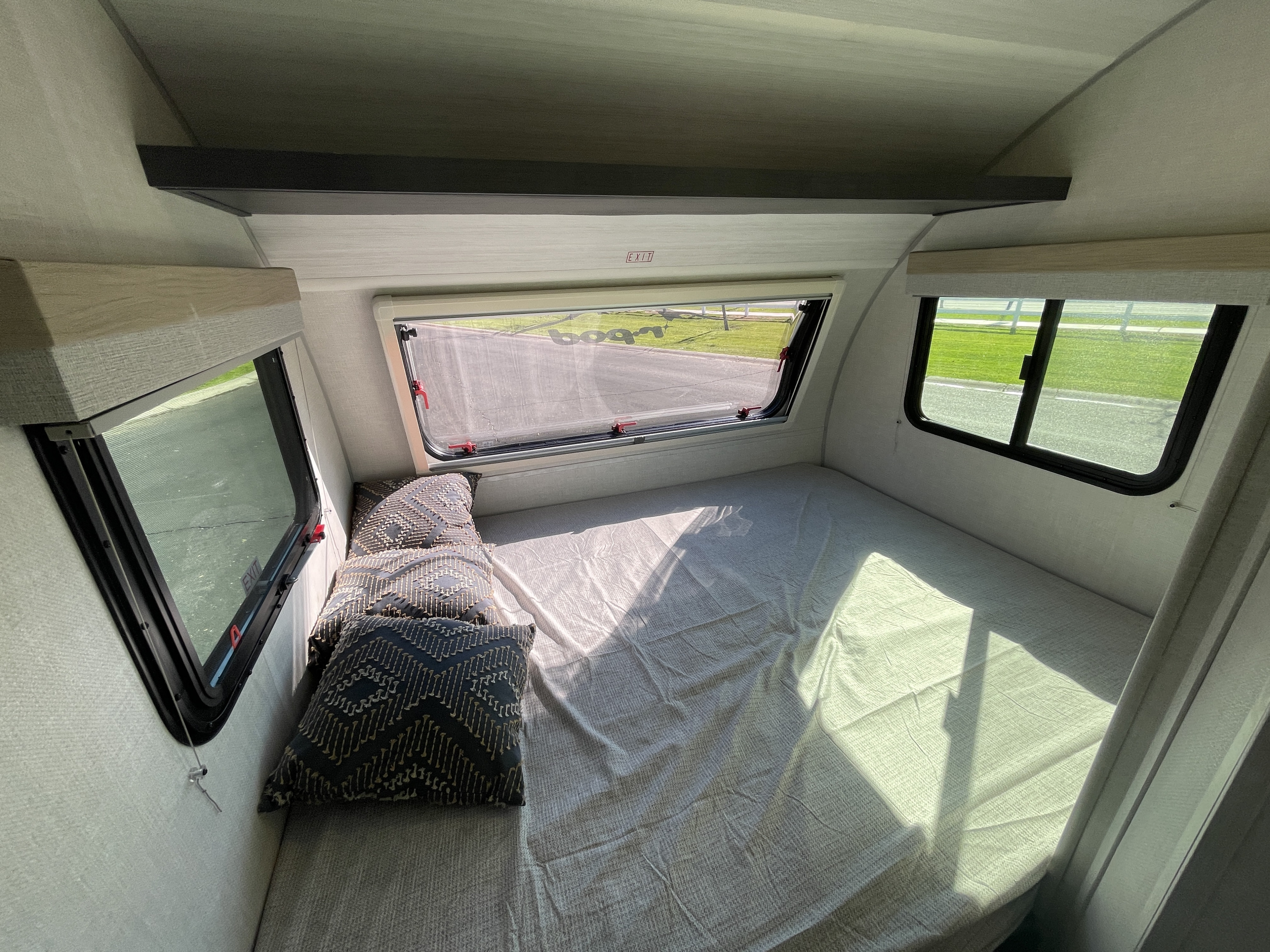 Spacious RV rental bedroom, featuring a large bed, multiple windows, and an overhead shelf, bathed in natural light.. Forest River R-Pod 2023