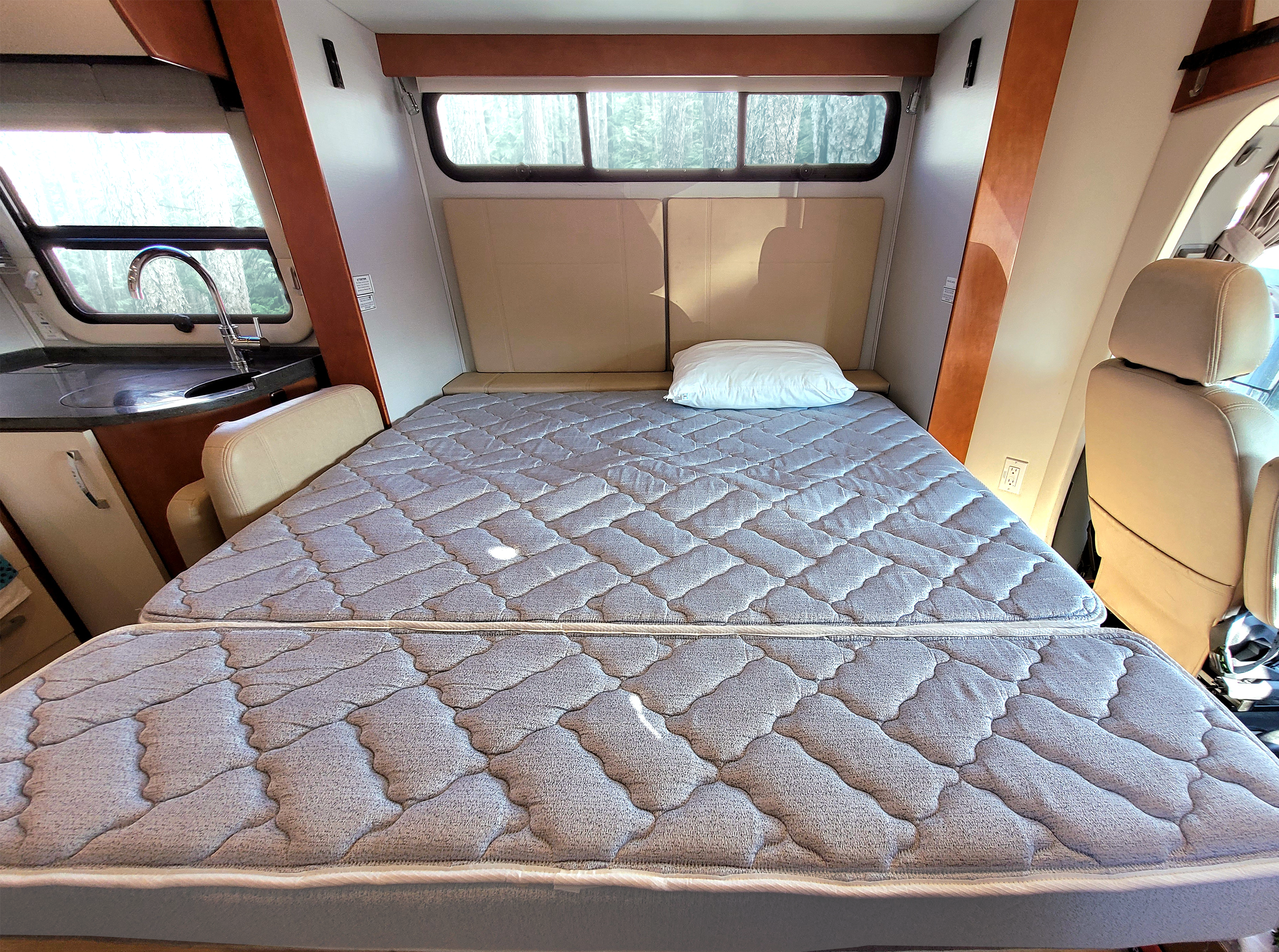 Inside a comfy rv rental, featuring a quilted convertible bed, small kitchen, and natural light from large windows.. Leisure Travel Unity 2017