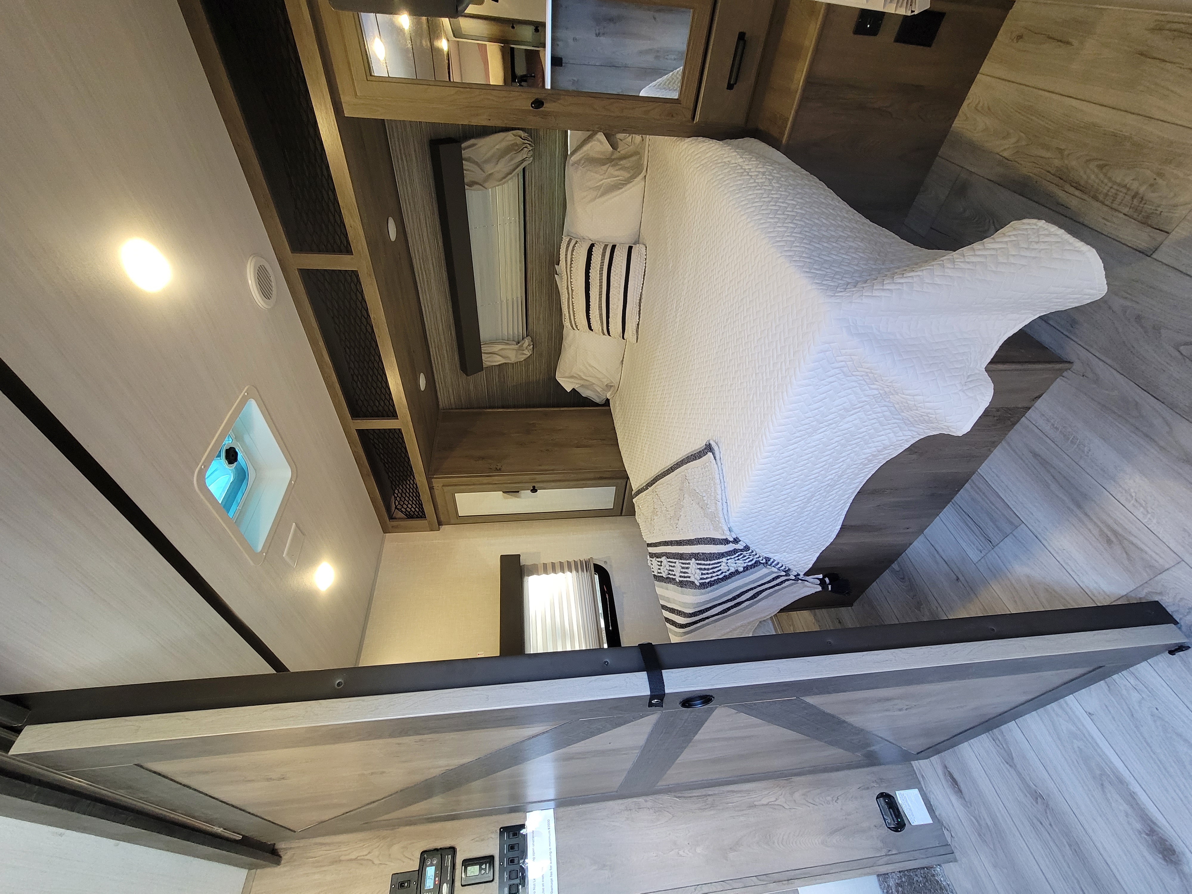 Cozy RV rental bedroom: white bed, striped accents, wood-style cabinets, and modern finishes. Ideal for travel comfort.. Forest River Surveyor 2022