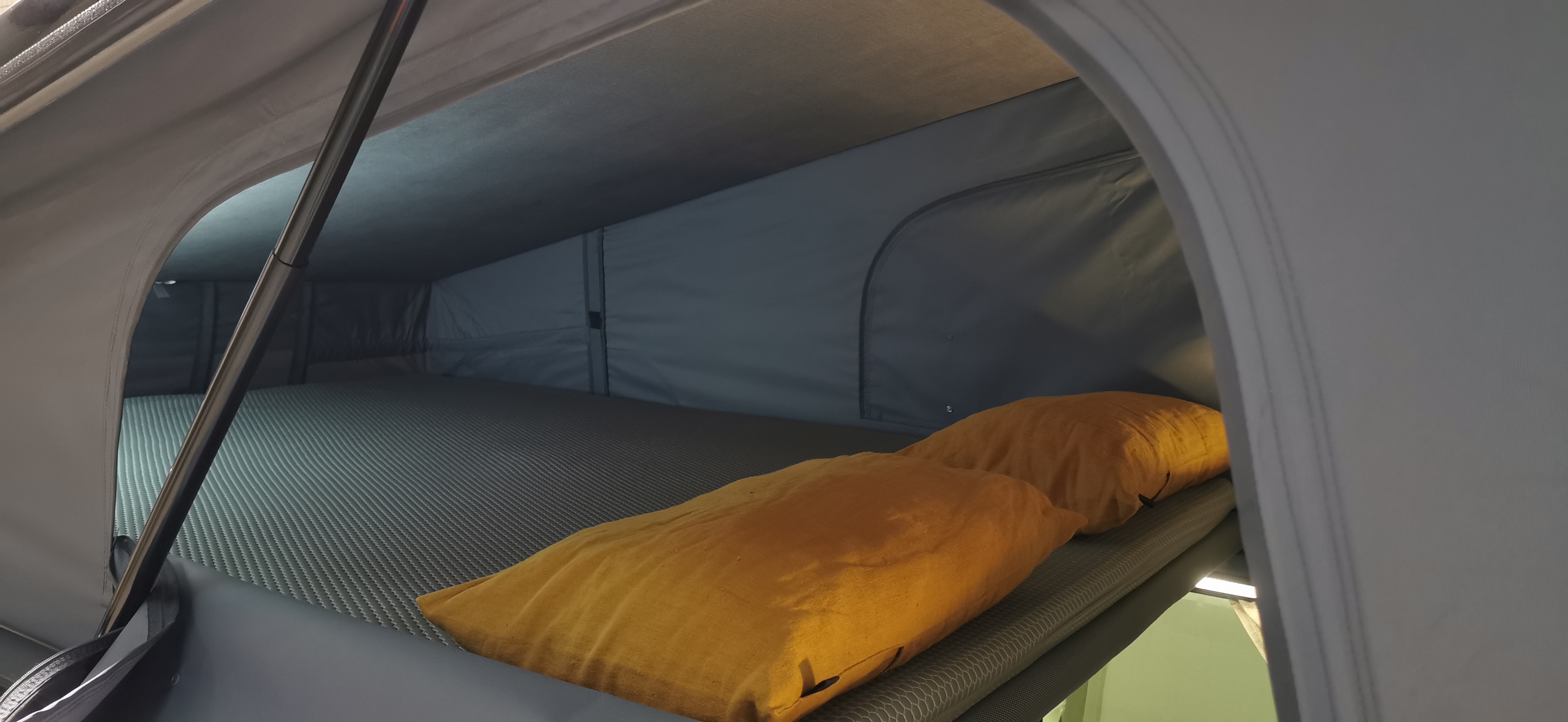 Interior of a cozy RV rental roof-top tent, featuring a textured bed with two soft orange pillows, ideal for camping.. Renault Trafic 2023