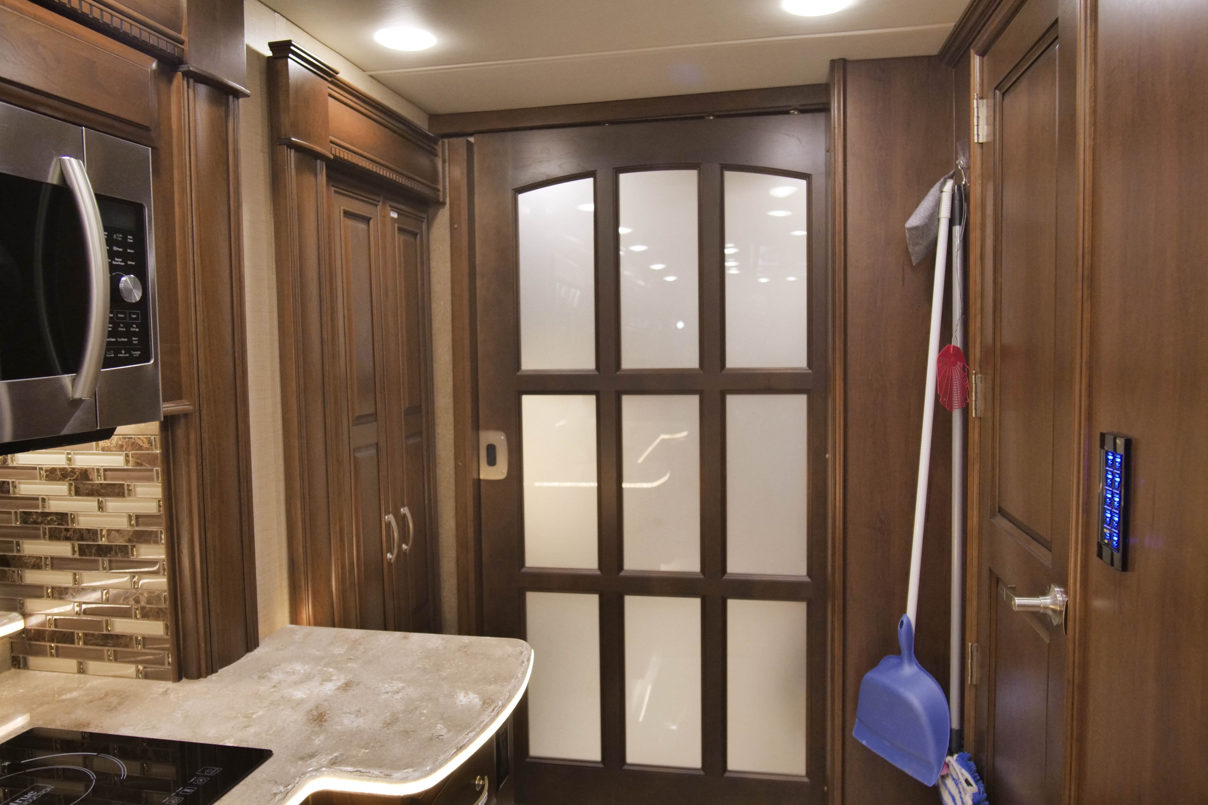 RV rental interior: microwave, kitchen counter with tiled backsplash, frosted glass door, and a control panel.. Entegra Coach Anthem 2016