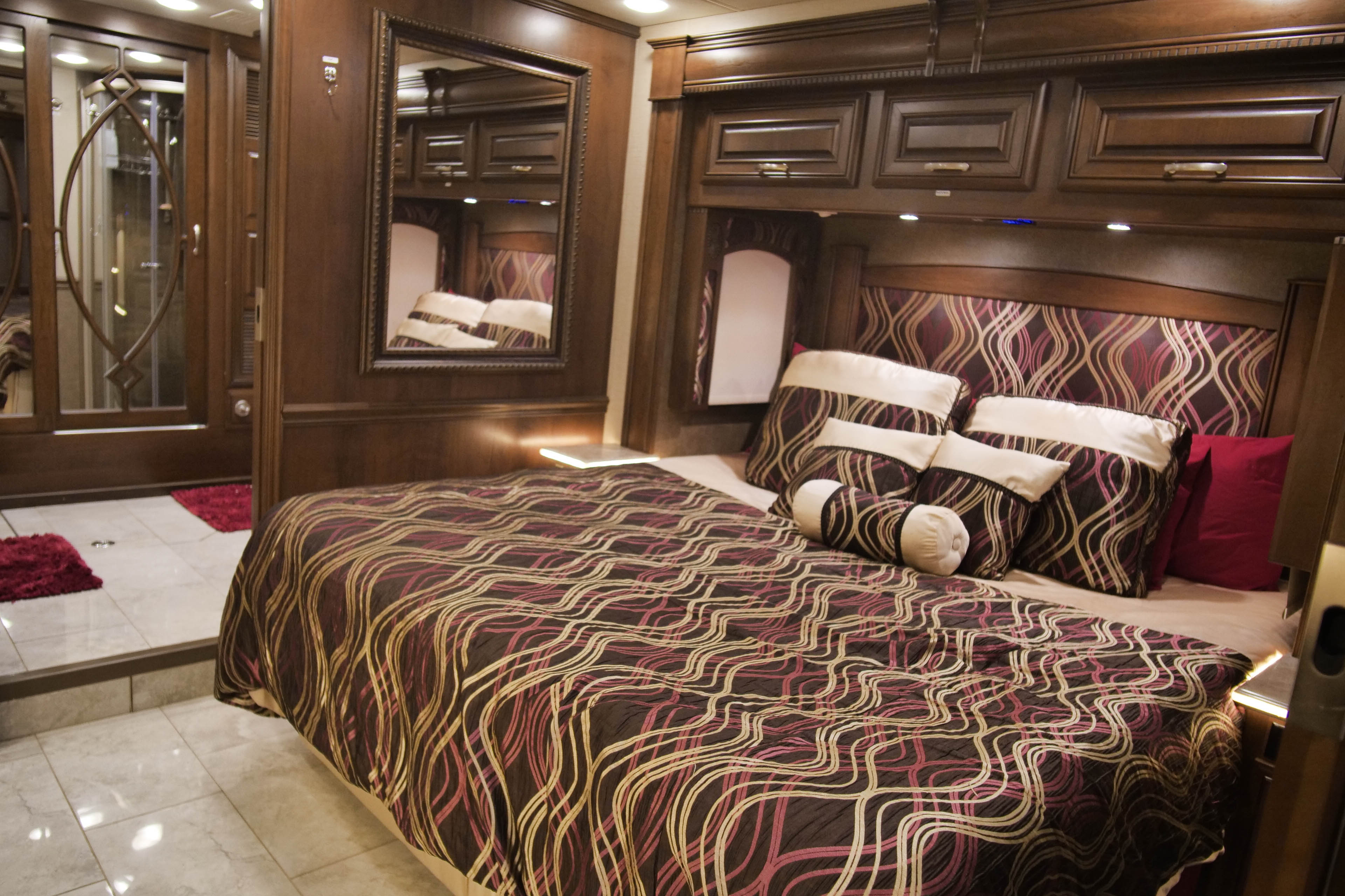 Luxurious RV rental bedroom with dark wood, patterned bedding, built-in storage, and mirror. Features a connected shower area.. Entegra Coach Anthem 2016