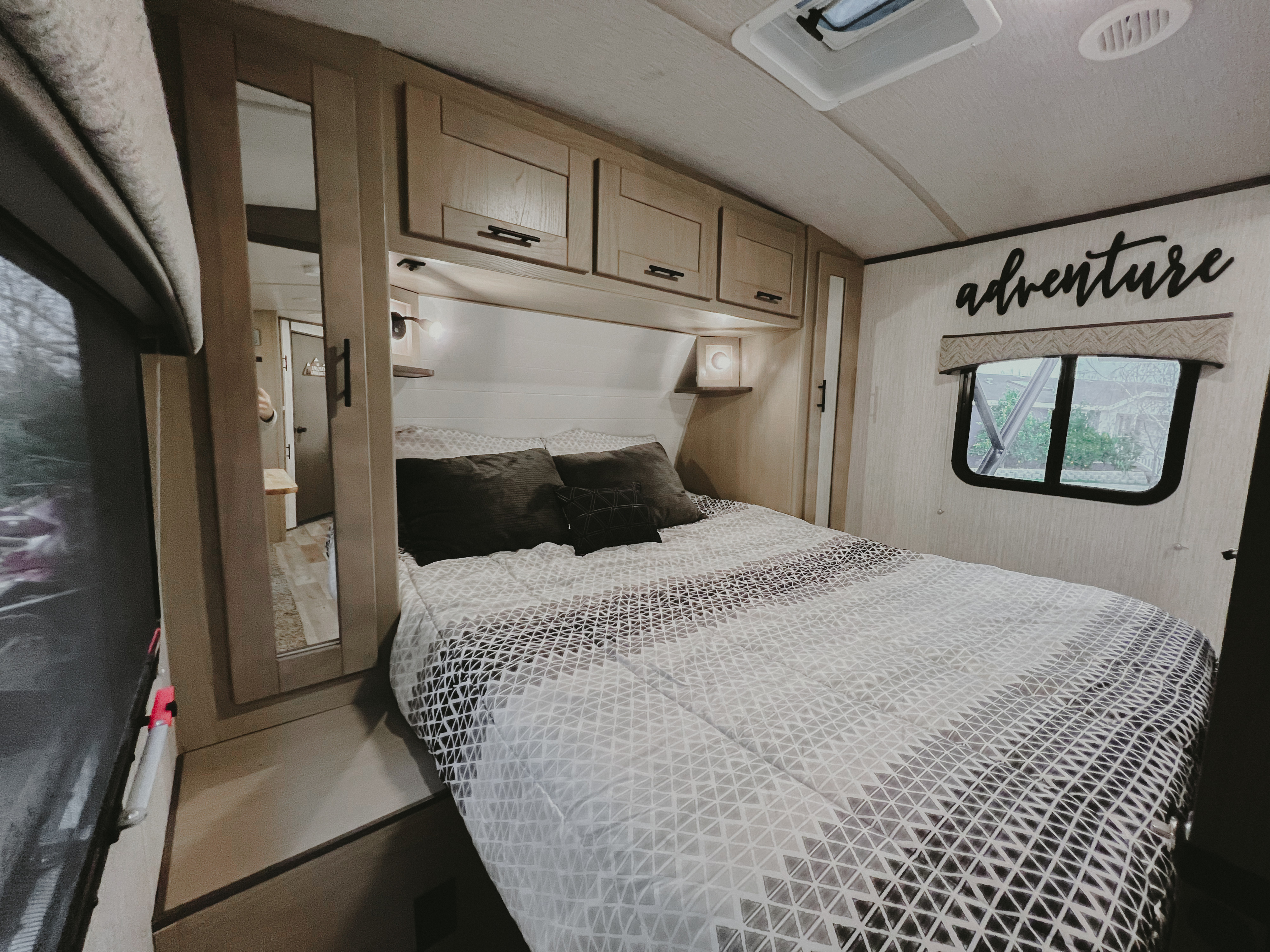 Cozy RV rental bedroom with a patterned comforter, overhead cabinets, and "adventure" wall decor.. Heartland RVs Sundance Ultra Lite 2021