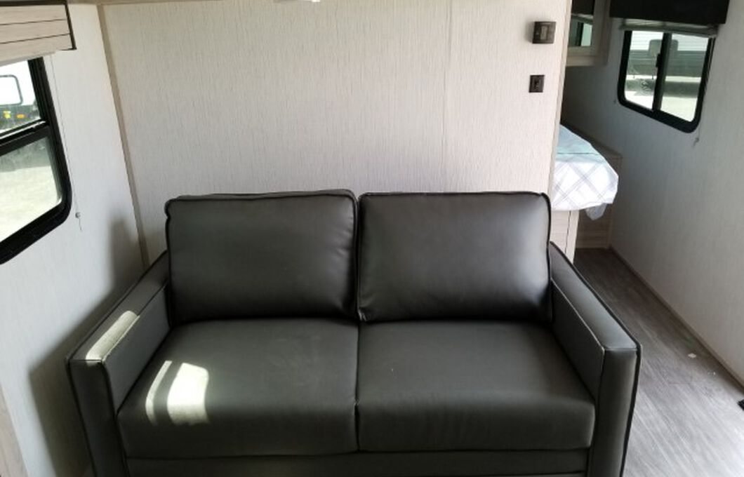 Gray sofa in an RV rental living area, with a window on left & compact sleeping space on right.. Cruiser RV Shadow Cruiser 2022