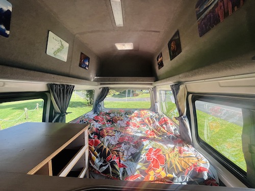Cozy RV rental camper interior with floral bed, practical storage, and window views. Ideal for mobile travel adventures.. Toyota Hiace 2014
