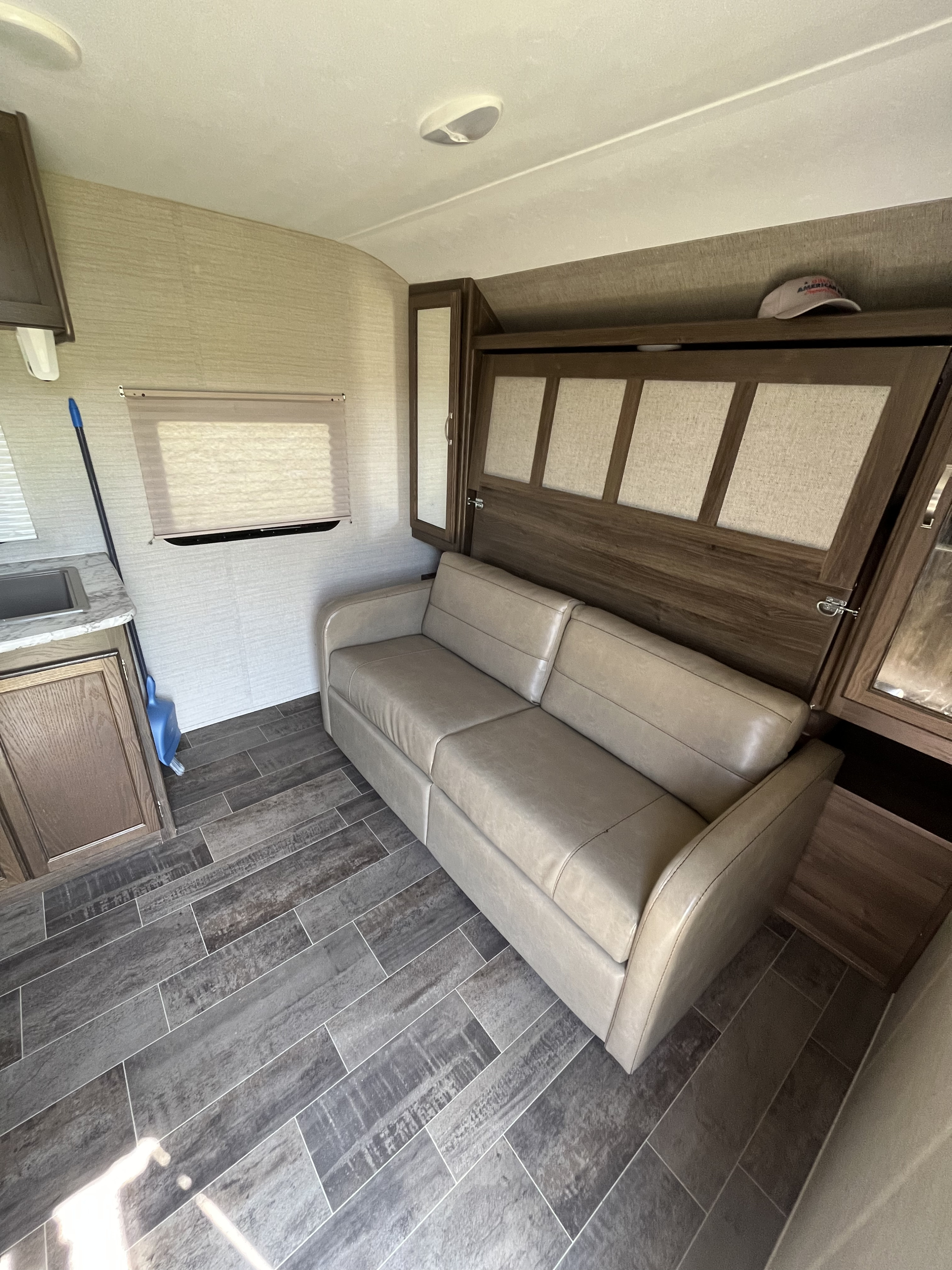 Cozy RV rental interior with a beige sofa, integrated Murphy bed frame, small kitchen, and wood-look flooring.. Keystone RV Bullet Crossfire 2018