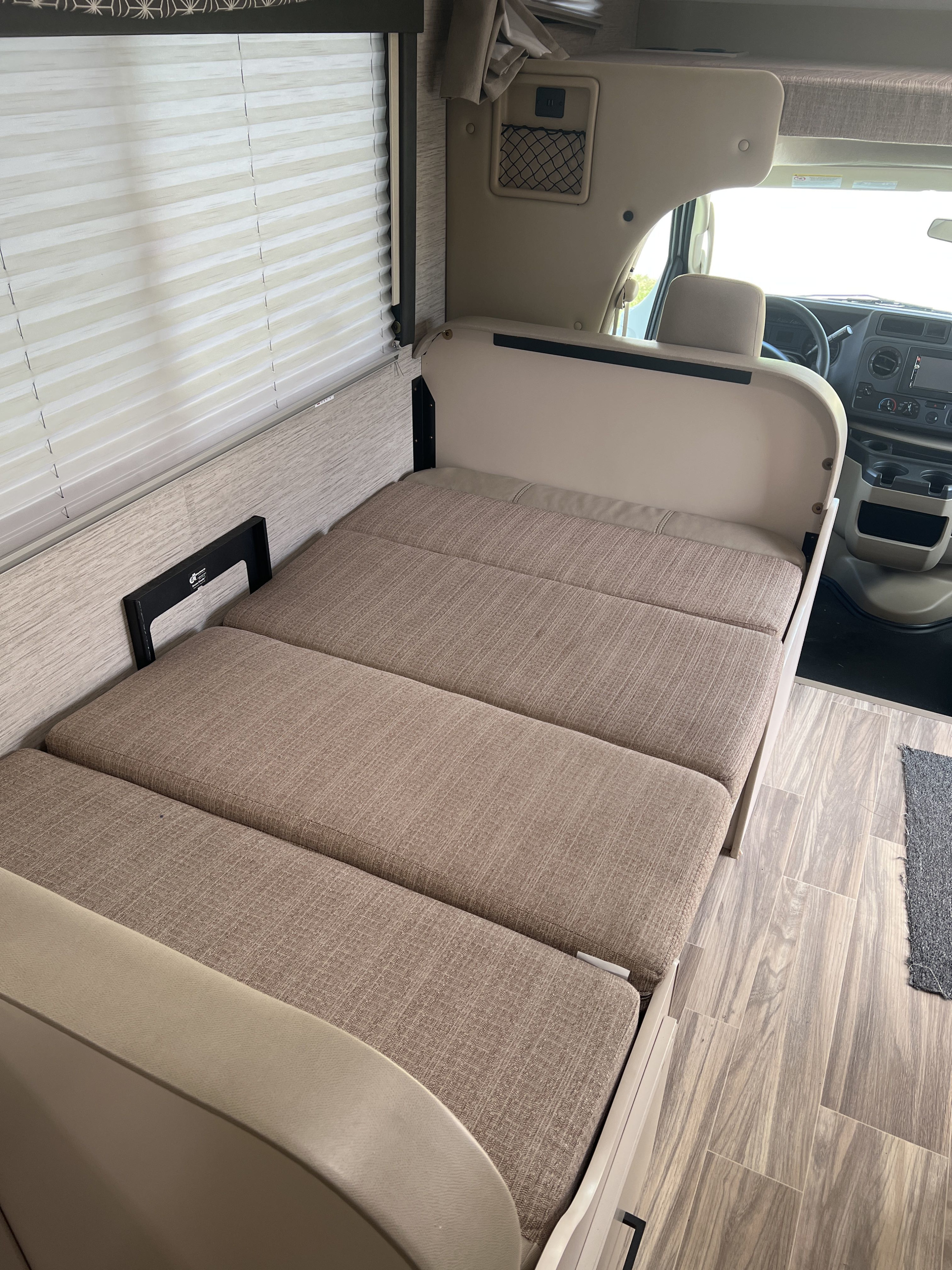 RV rental living space: Cushioned convertible bed/seating, window blinds, storage net, and driver's cabin.. Thor Freedom Elite 2022