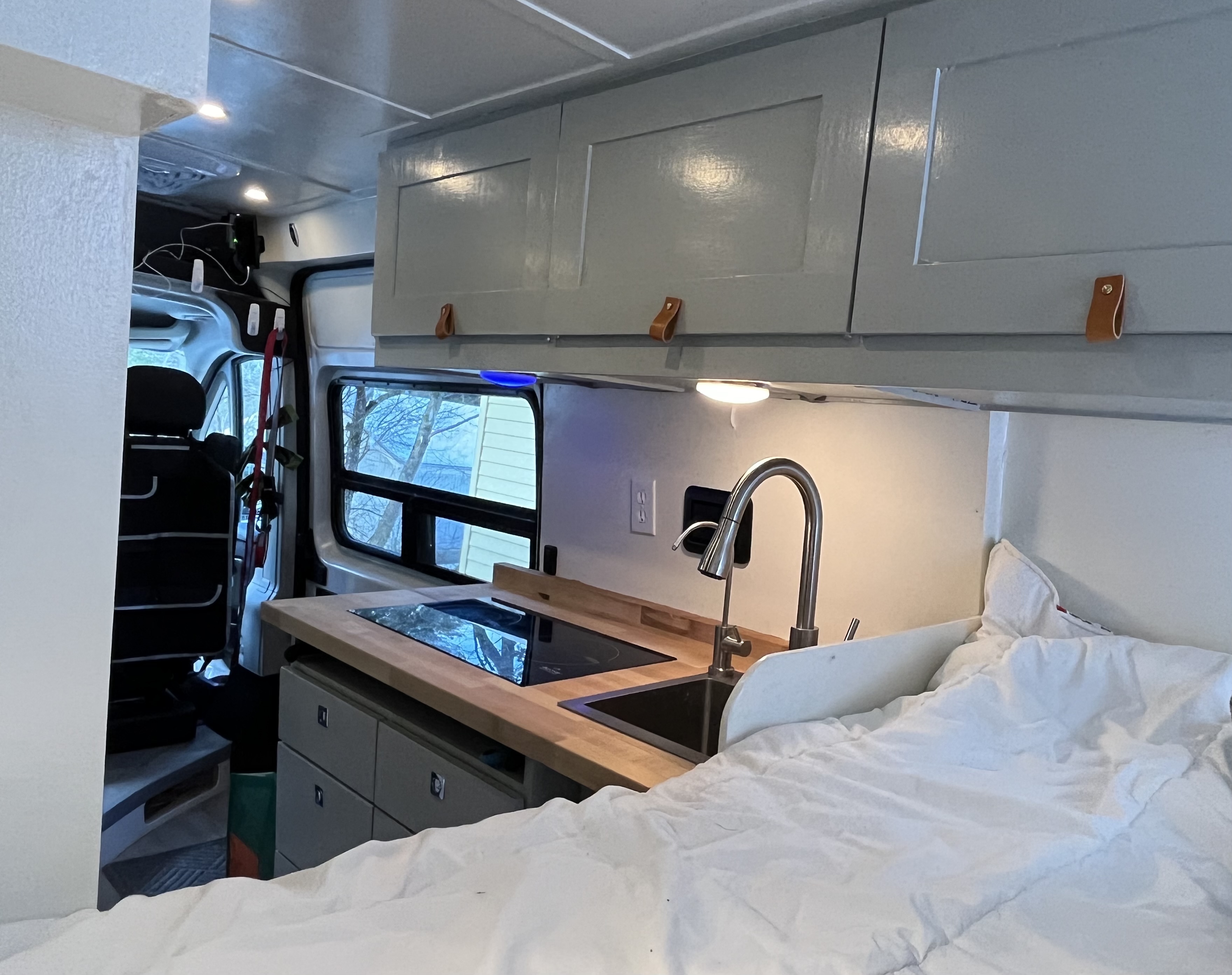 Inside an rv rental: functional kitchenette with cooktop & sink, comfy bed, and ample overhead cabinets.. Ram Promaster 2022