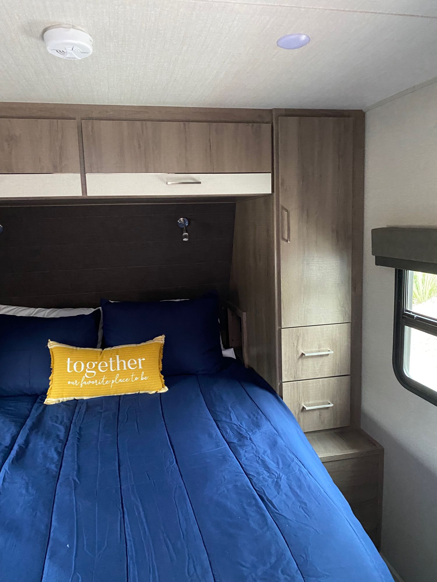 Cozy RV rental bedroom with a blue bed, built-in storage, and a yellow "together" pillow for a homey feel.. Other Other 2023