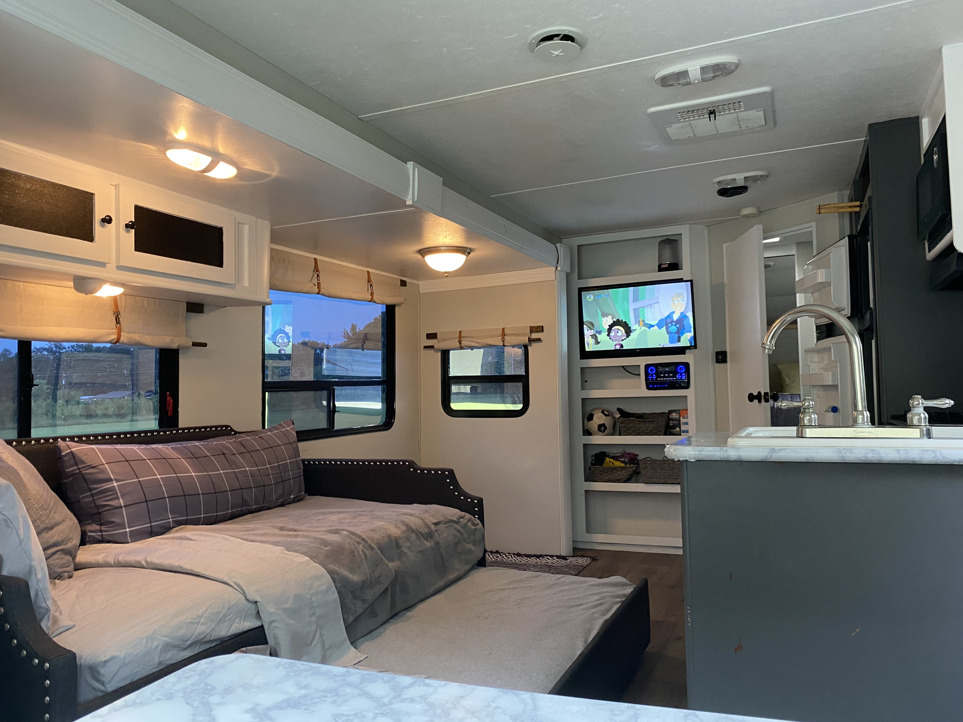 Cozy RV rental interior featuring a living area with TV, daybed, shelving, and a kitchen sink, ideal for comfortable travel.. Aspen Trail Aspen Trail Trailer 2015