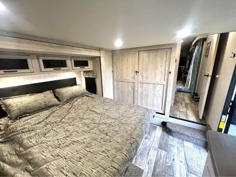 Spacious RV rental bedroom featuring a comfortable bed with grey bedding, overhead storage, and modern wood interior.. Forest River Sandpiper 2022