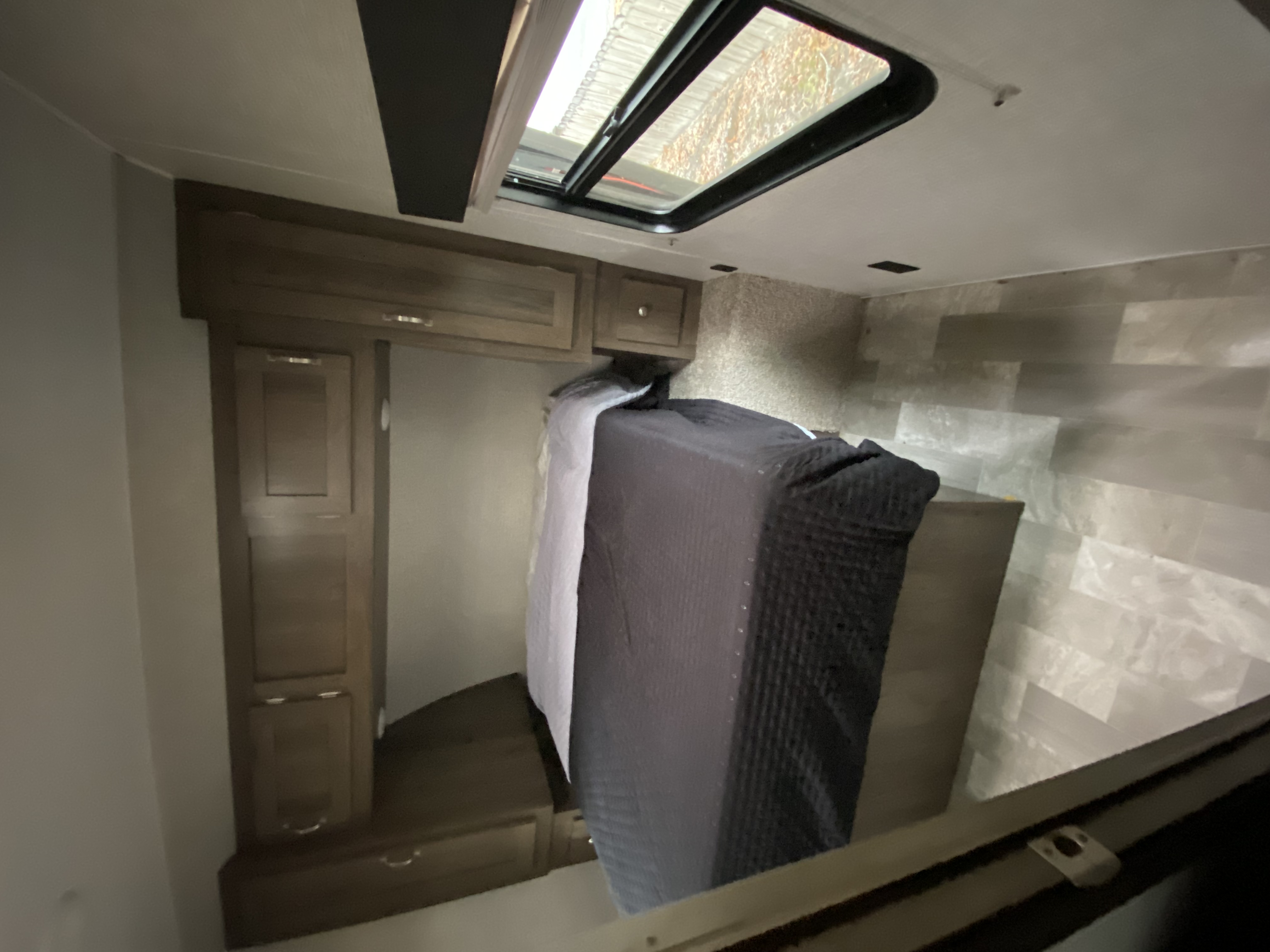 Inside an RV rental: a compact bedroom features a bed, wood-look cabinets, and a bright ceiling skylight.. East to West Della Terra 2021