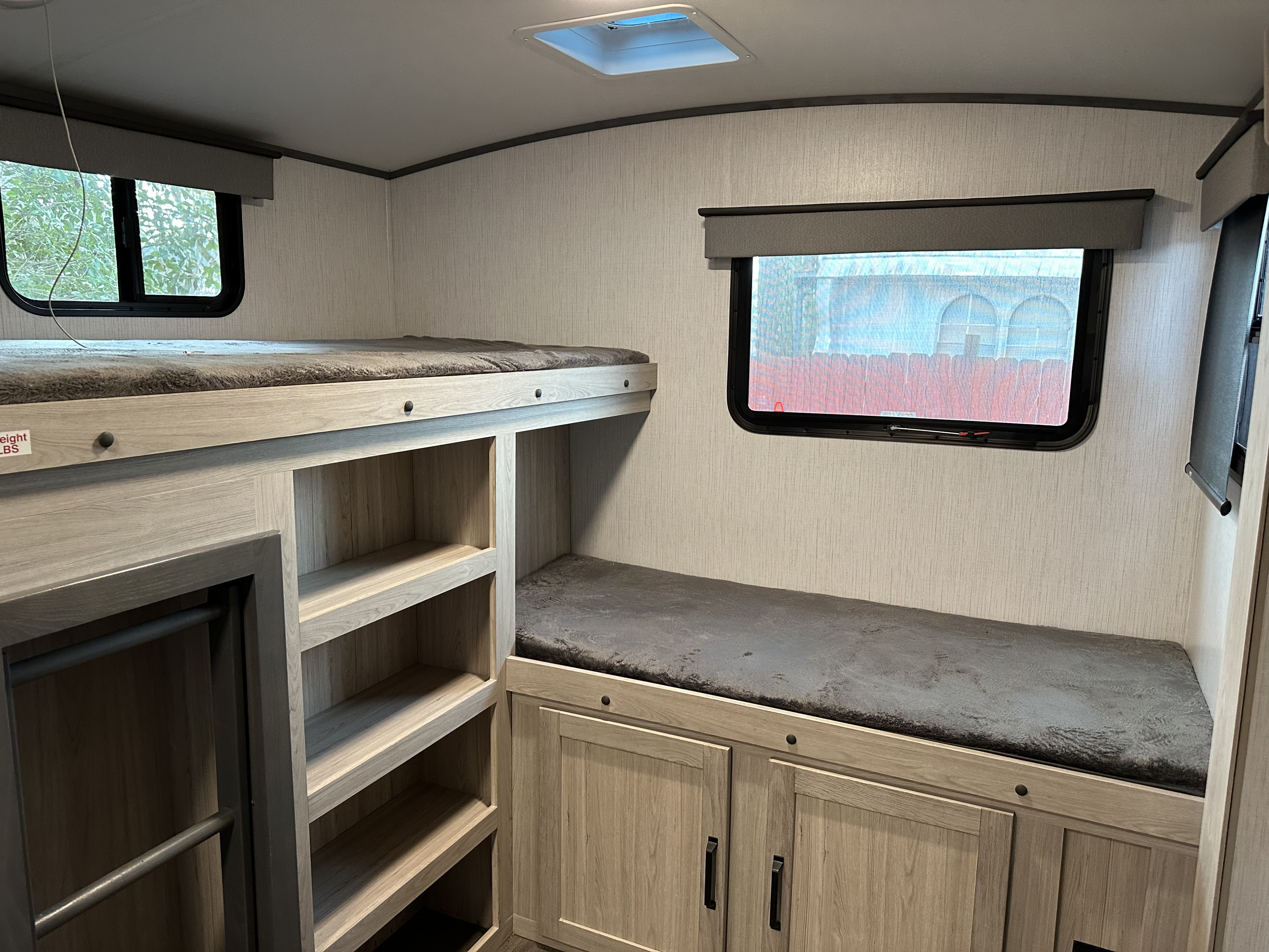 RV rental bunk room with light wood storage shelves, two beds with grey cushions, and large windows.. Twilight RVS Signature 2022