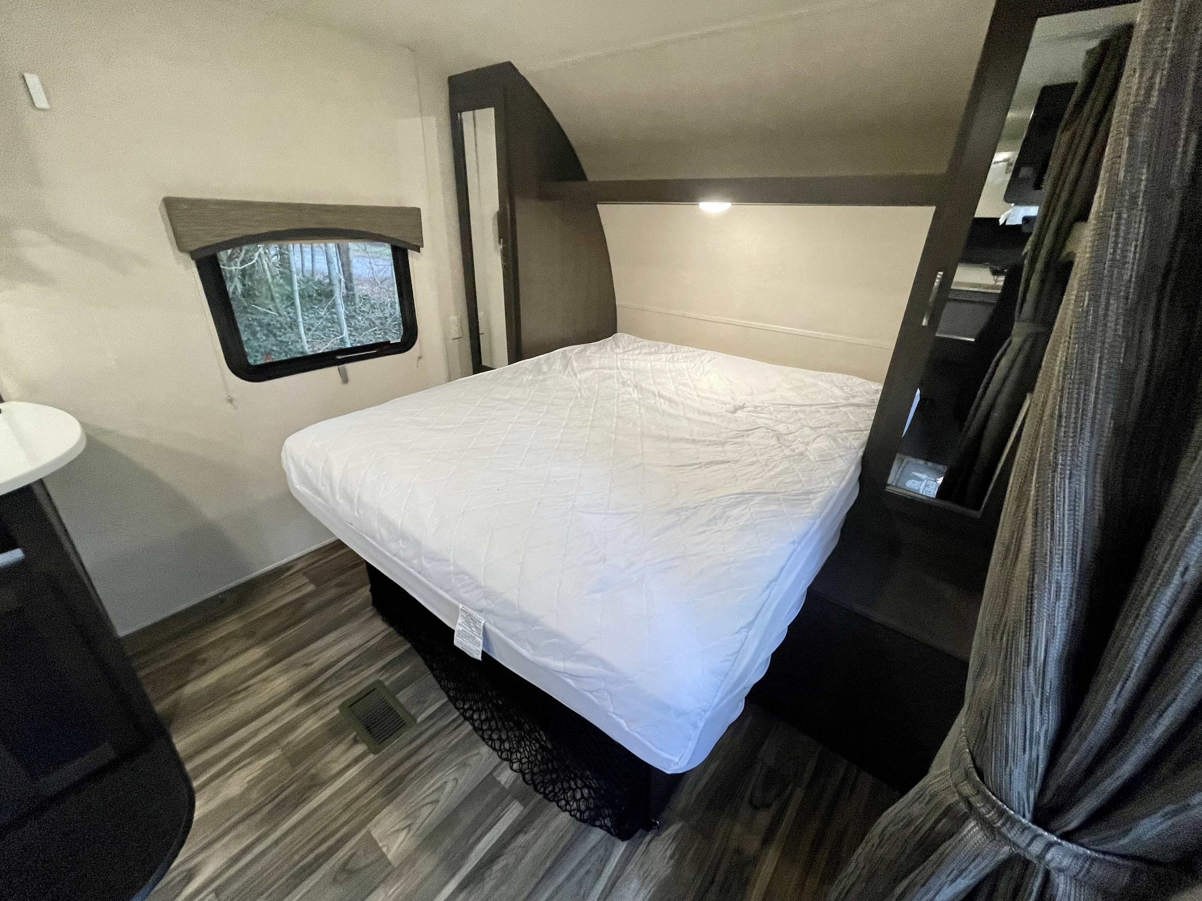 View of an RV rental bedroom with a neatly made white bed, a window with outdoor view, and dark built-in cabinetry.. Forest River EVO T2250 2019