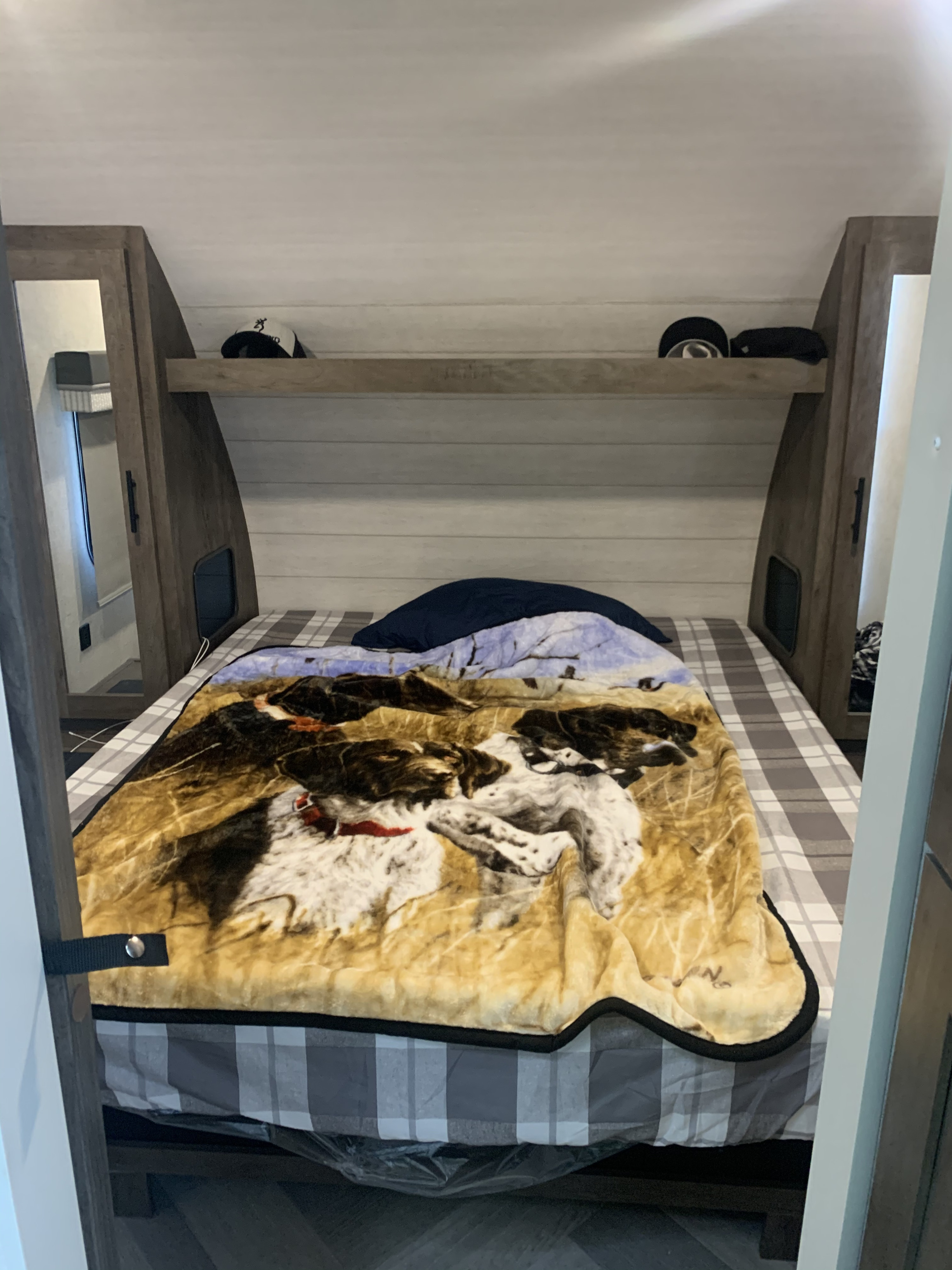 Cozy RV rental bedroom with dog blanket, plaid bedding, and overhead shelf. Perfect for your next adventure.. Forest River Wildwood X-Lite 2021