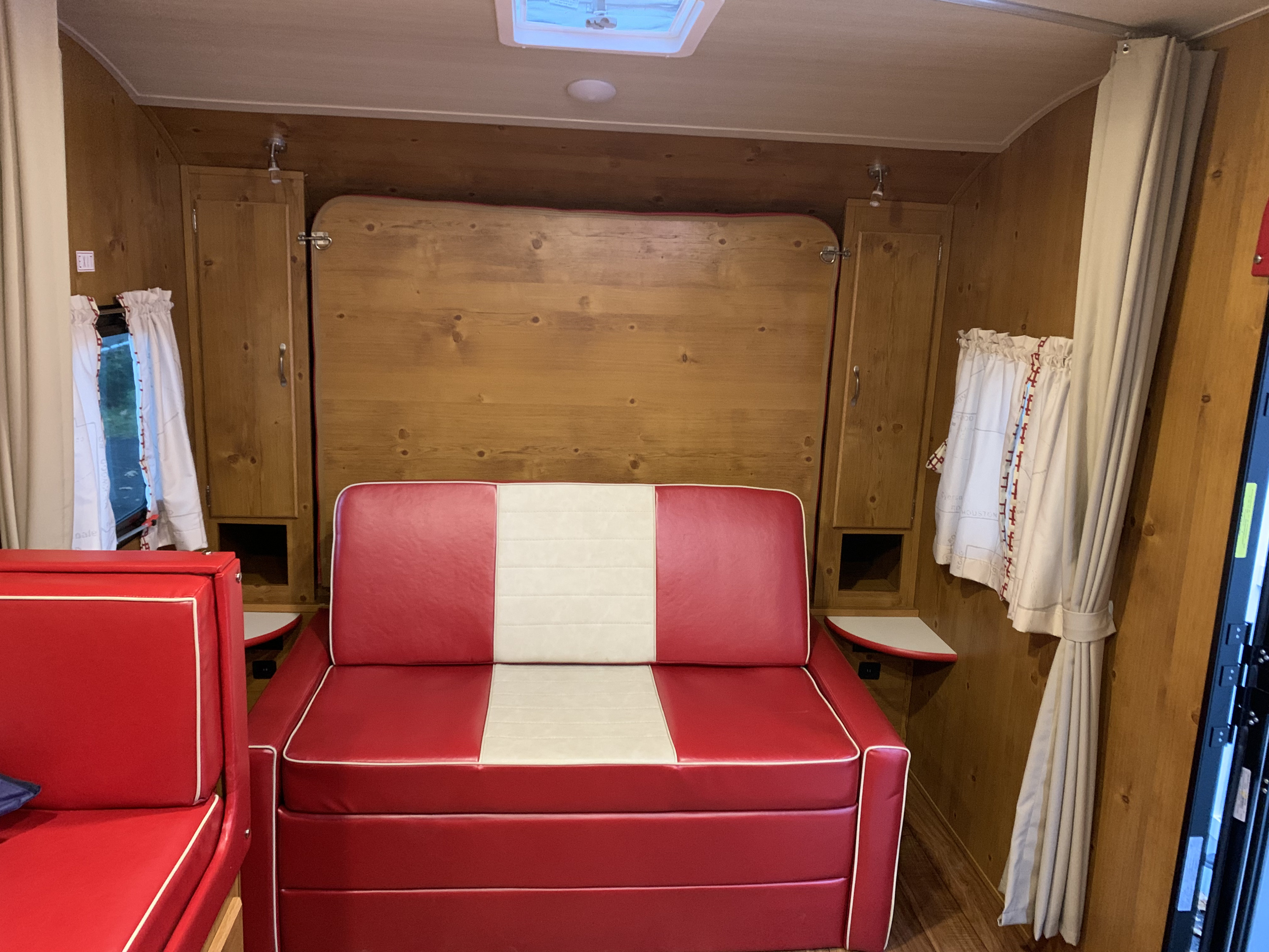 Spacious rv rental interior features a red/white sofa, wood paneling, and a fold-down bed. Ideal camper living.. Gulf Stream Vintage Cruiser 2021