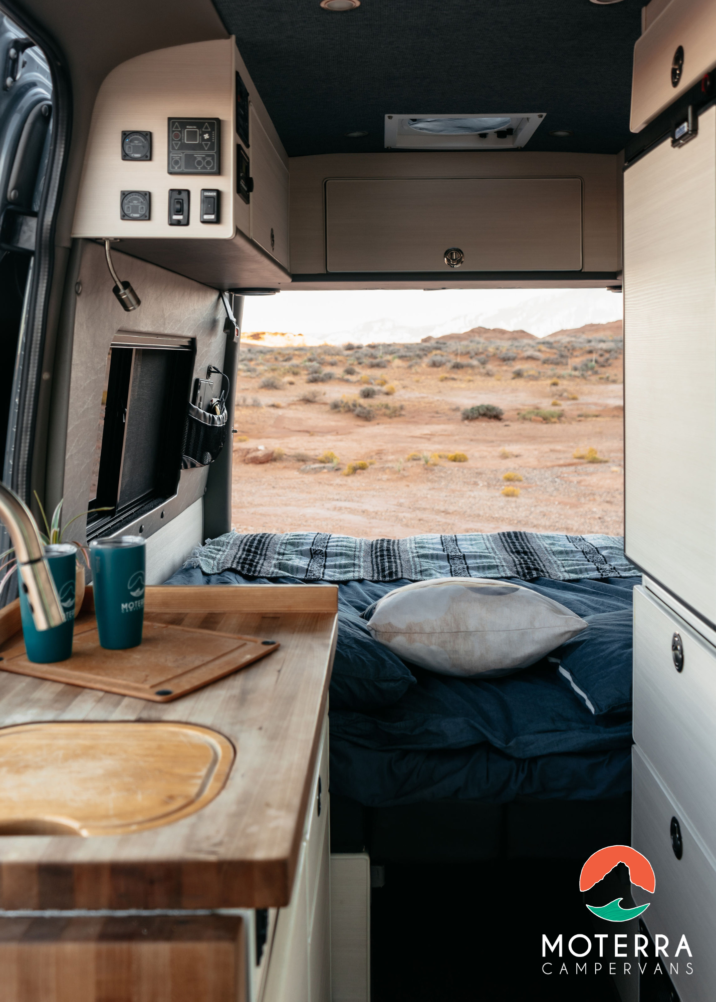 Spacious RV rental interior featuring a functional kitchen, comfortable bed, and stunning desert view from the open rear doors.. Mercedes-Benz Sprinter 2021