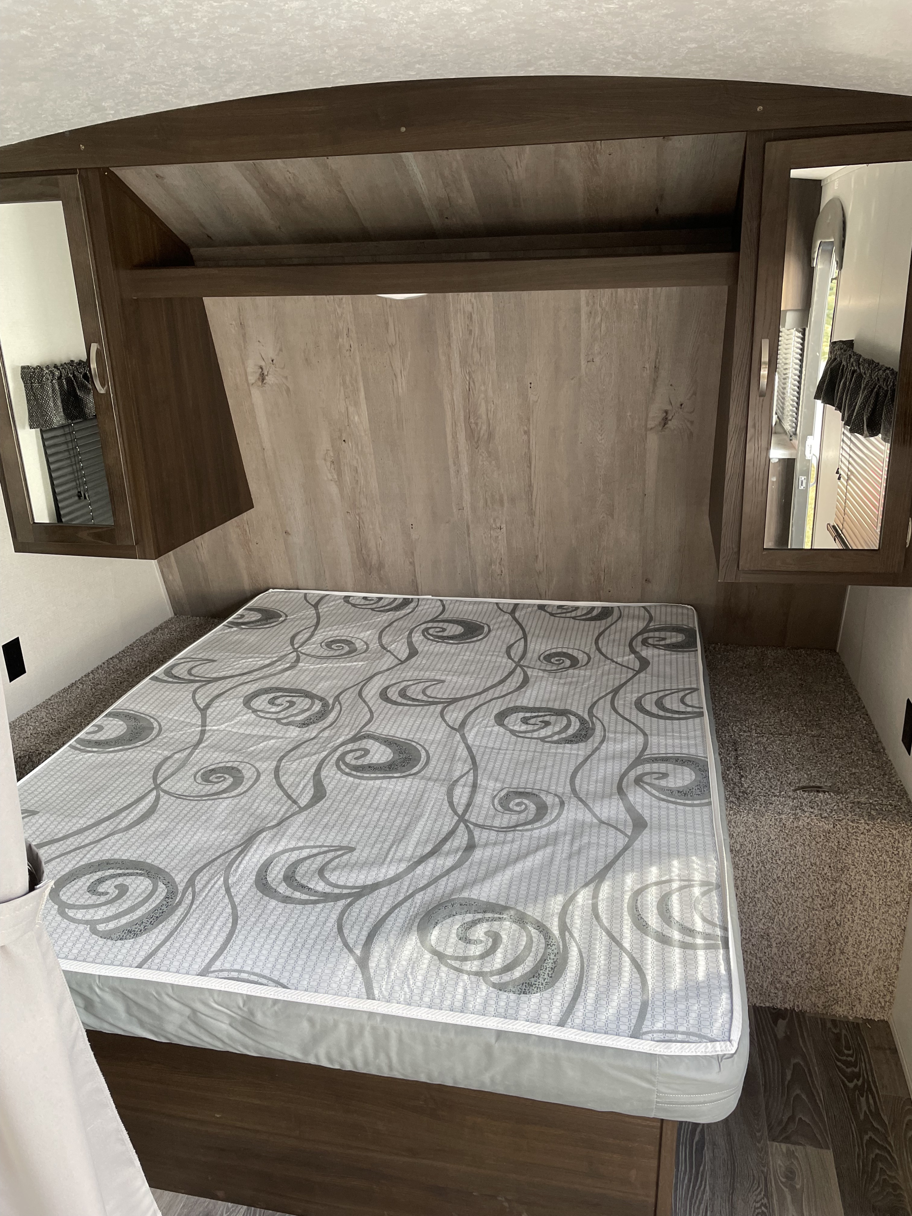 Cozy RV rental bedroom featuring a patterned mattress, overhead storage, and integrated mirror cabinets.. Keystone RV Springdale 2020