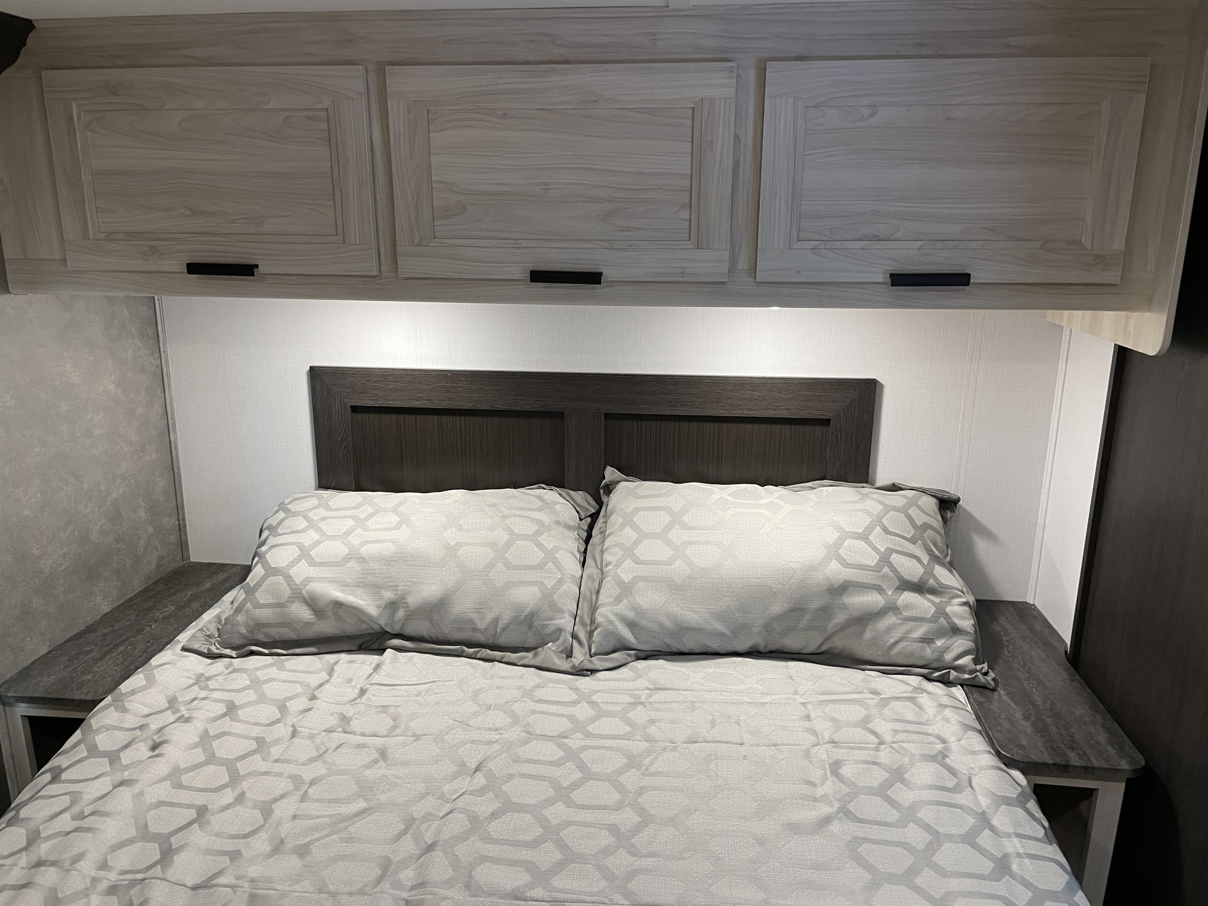 Cozy RV rental bedroom featuring modern grey bedding, a dark headboard, and light wood overhead cabinets for storage.. Forest River Forester 3251DSF 2023
