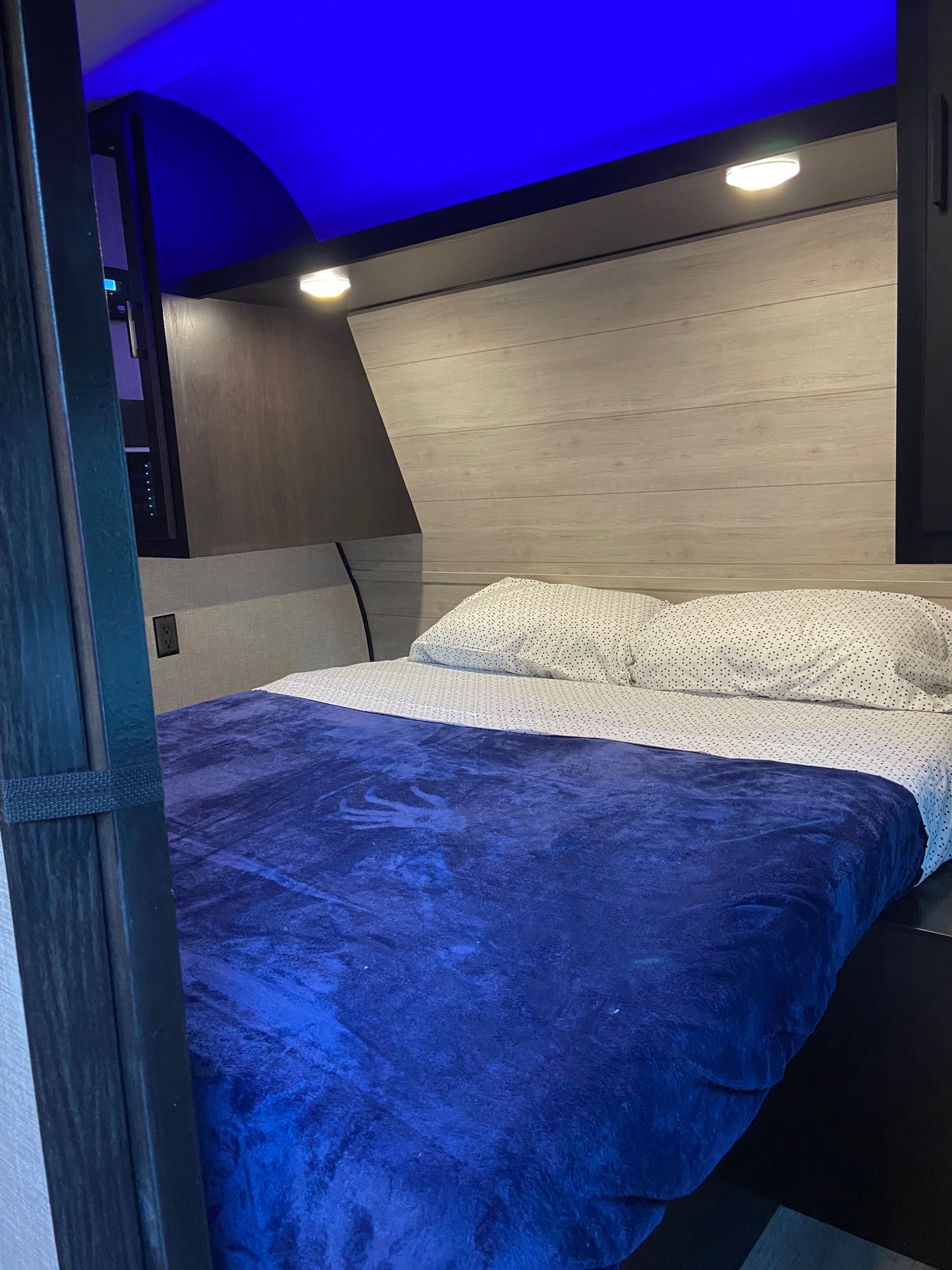 Cozy RV rental bedroom featuring a bed with blue blanket, accent lighting, and modern wood paneling. Ready for adventure!. Jayco Jay Flight SLX 2022