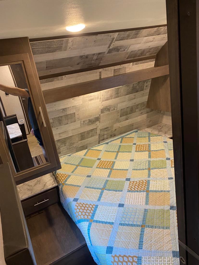 Cozy RV rental bedroom featuring a patterned quilt, wood paneling, and built-in storage on the left.. Dutchmen Coleman Lantern 2019