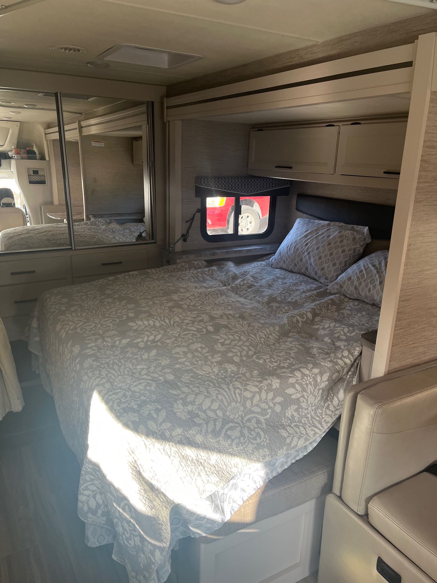 Cozy RV rental bedroom with a comfy bed, mirrored wardrobe, overhead cabinets, and natural light.. Thor Gemini 2022