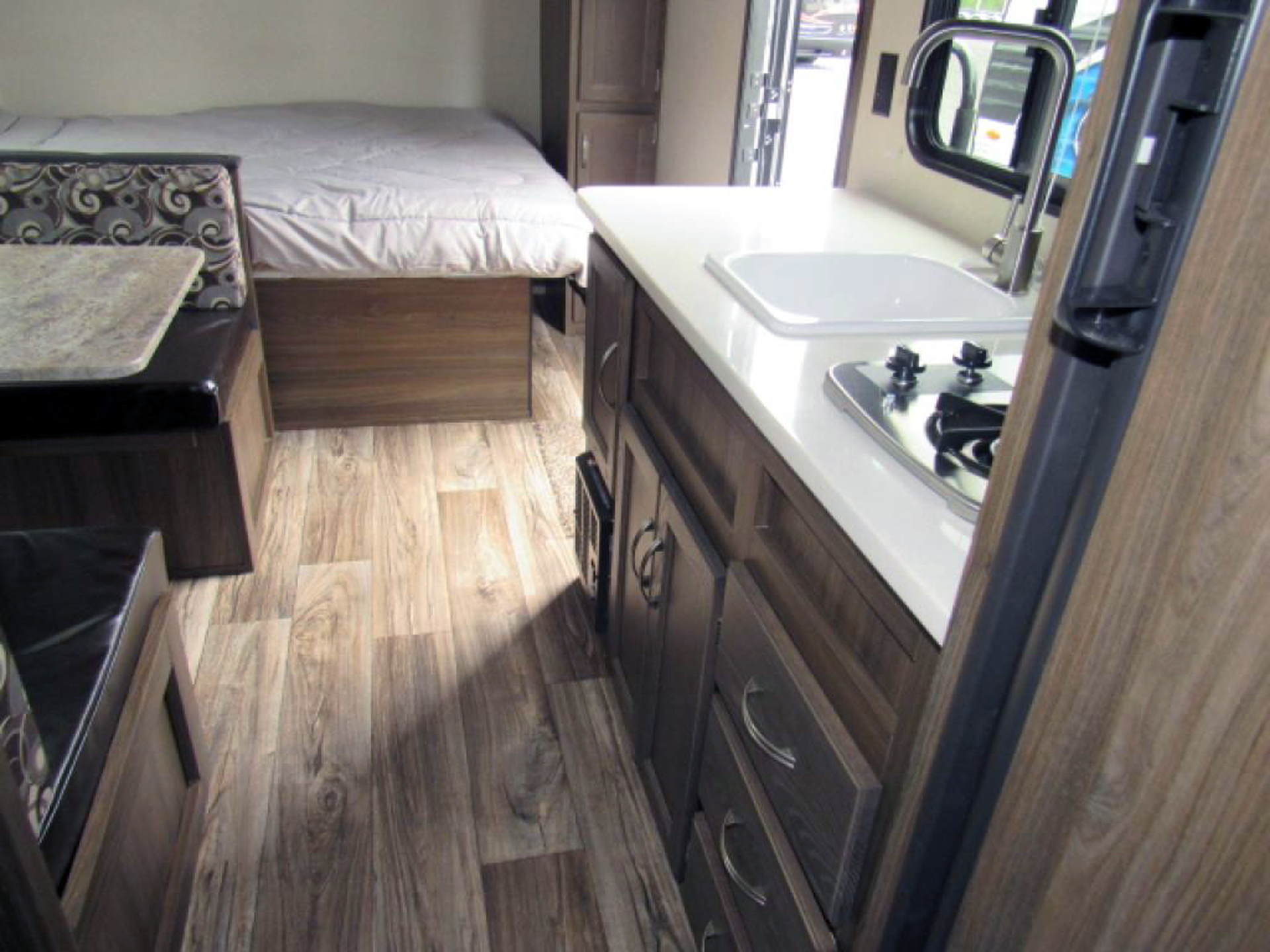 RV rental interior: compact kitchen with stove & sink, dinette, and bed area, all on wood flooring.. Riverside Rv Dream 175BH 2018