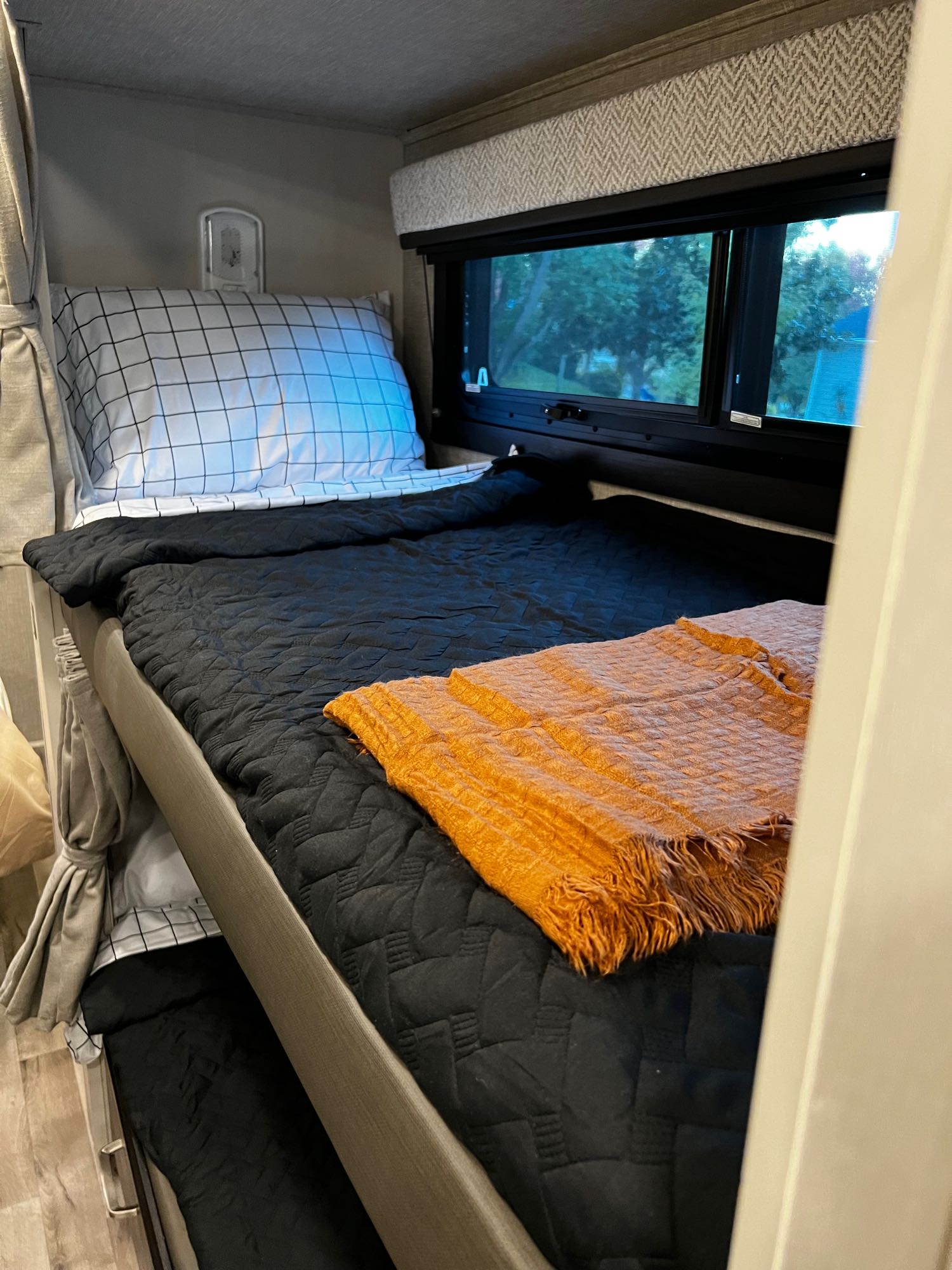 Cozy RV rental bunk beds, fully made with patterned bedding. The top bunk has a window view and an orange throw blanket.. Entegra Coach Odyssey 31F 2023