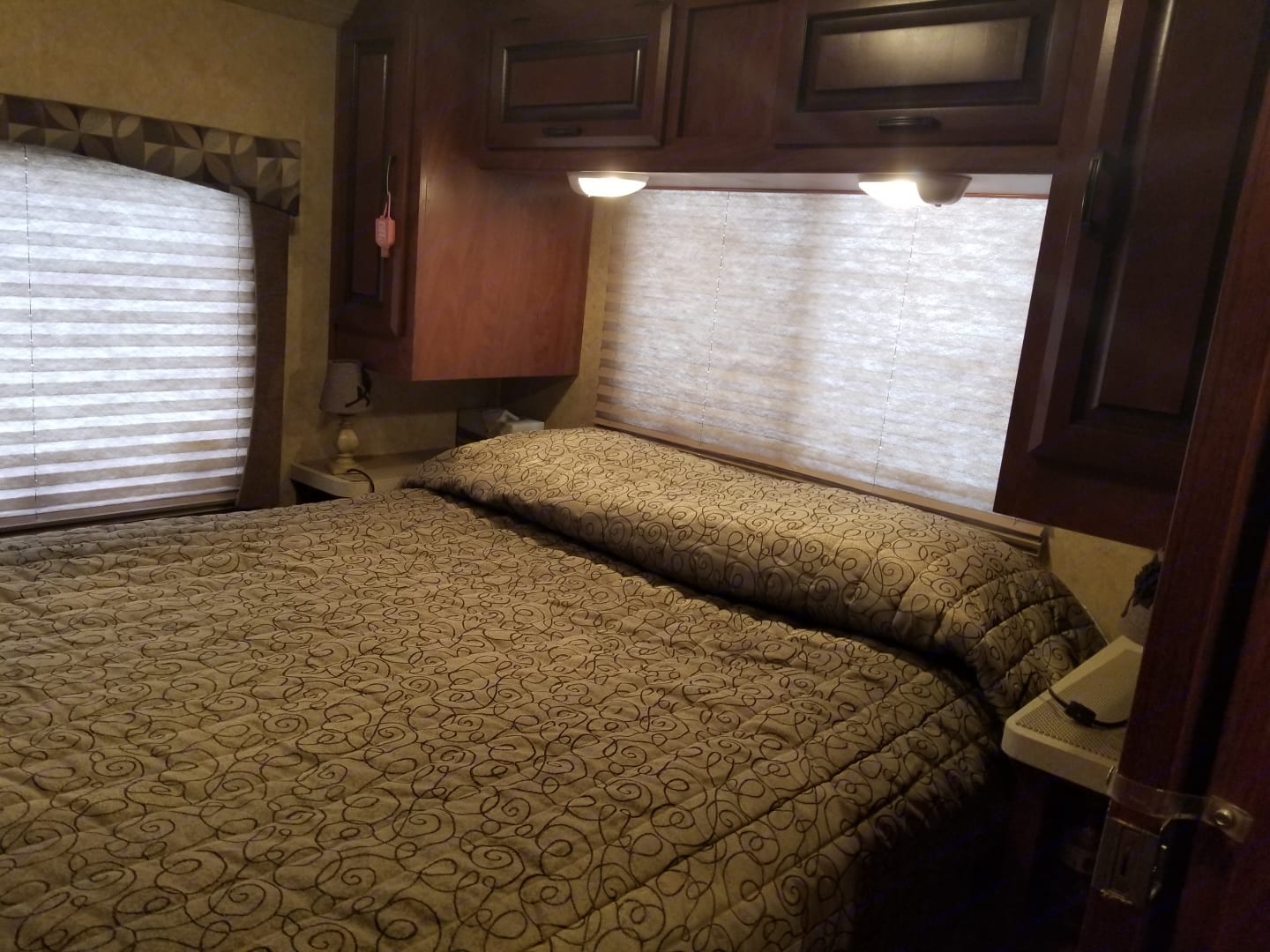 Cozy RV rental bedroom features a patterned bed, blinds, overhead cabinets, and nightstands for your travel comfort.. Forest River Sunseeker 2013