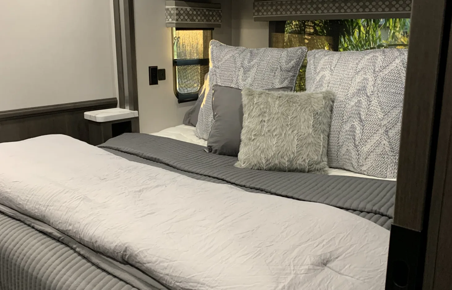 Cozy RV rental bedroom featuring a comfortable bed with gray and white bedding, various decorative pillows, and a small nightstand.. Georgetown GT5 2021