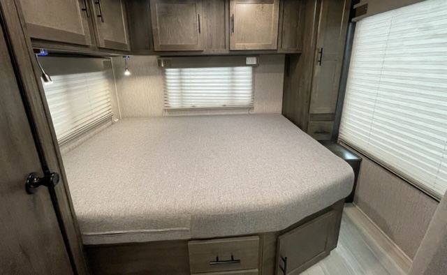 Cozy RV rental bedroom features a comfy bed, overhead storage cabinets, and bright windows with blinds for peaceful nights.. Other Leprechaun 2022