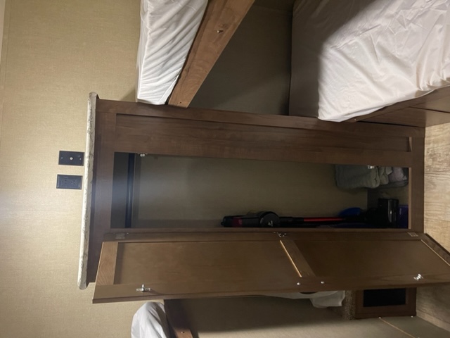 RV rental interior: bunk beds, a central wooden storage cabinet with an open compartment storing a vacuum, and open lower doors.. Gulf Stream Kingsport 2019